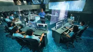 A high-tech control room with multiple people in business casual attire working at computer stations. A man stands in the center pointing at a holographic display, as large wall screens show various data visualizations and cityscape images, perfect for an exhibition promotion or construction video backdrop.