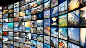 A large curved wall filled with numerous screens displays a variety of images, including landscapes, landmarks, nature scenes, airplanes, cityscapes, animals, buildings, and night skies. This vibrant collage creates a stunning visual experience perfect for a video production house.