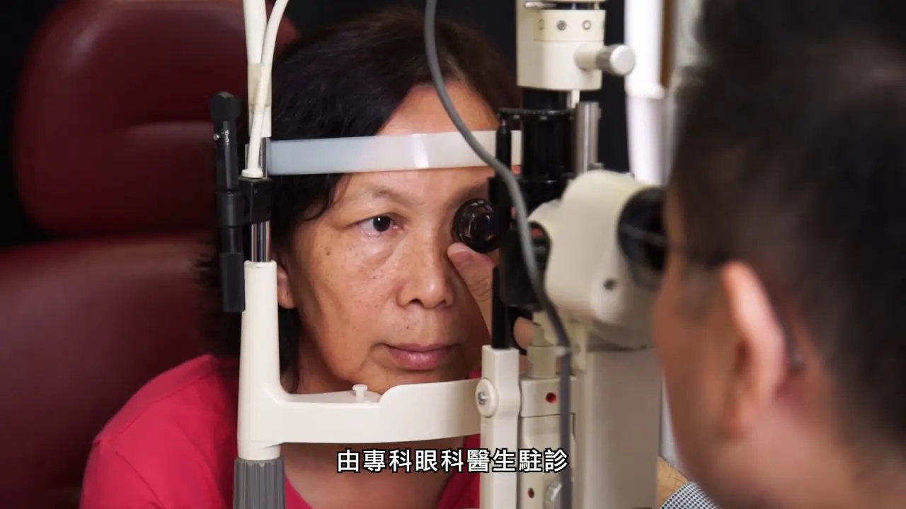 A woman is sitting in front of an eye examination device, focusing on a lens as an eye specialist examines her vision. She appears attentive, wearing a red top. The specialist's back is visible in the foreground. Chinese text is displayed at the bottom, highlighting this moment from an exhibition promotion.