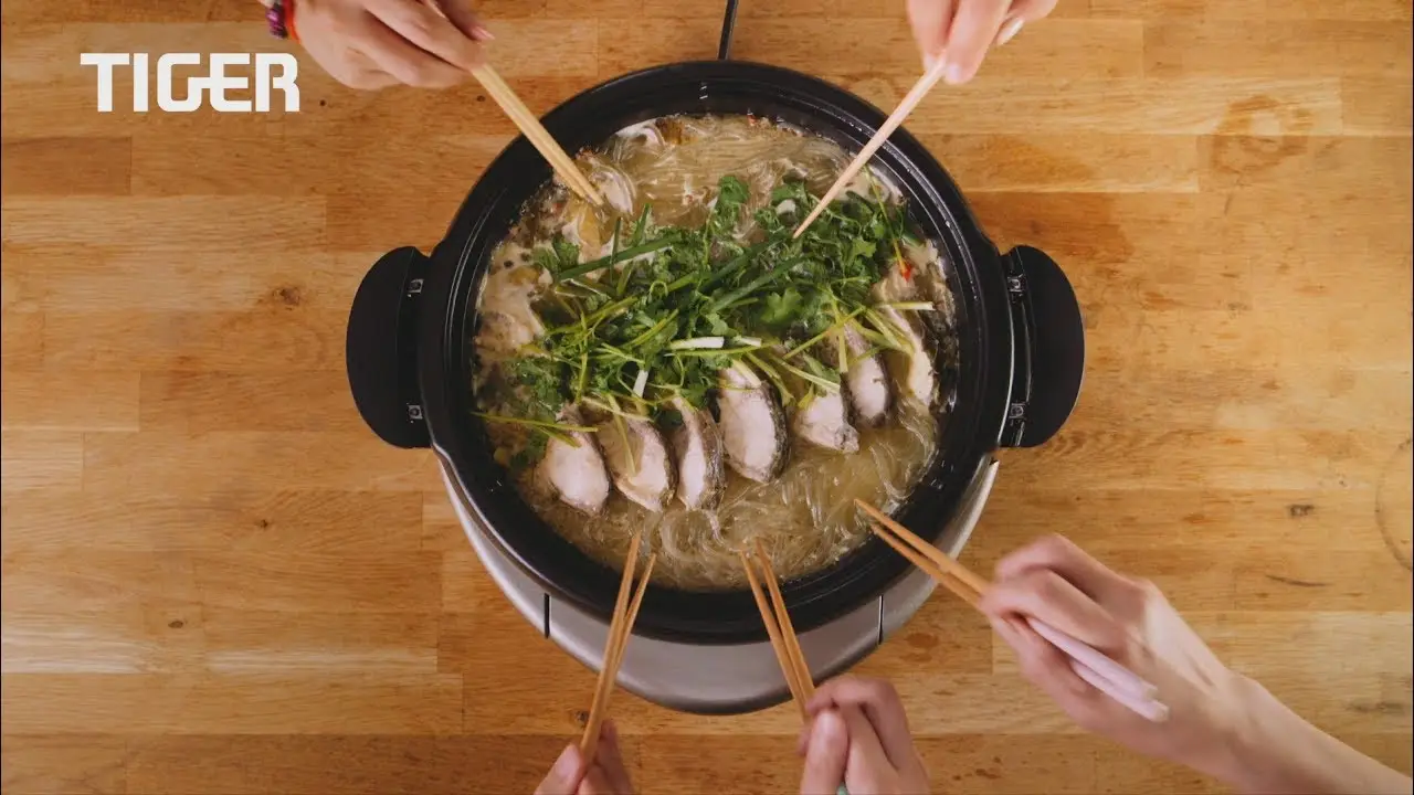 Four pairs of hands holding chopsticks reach into a pot placed on a wooden table. The pot contains broth, noodles, green onions, and slices of meat. Perfect for capturing in an Animation or for a Video Production House to showcase culinary creativity. The word "TIGER" is visible on the left side of the image.