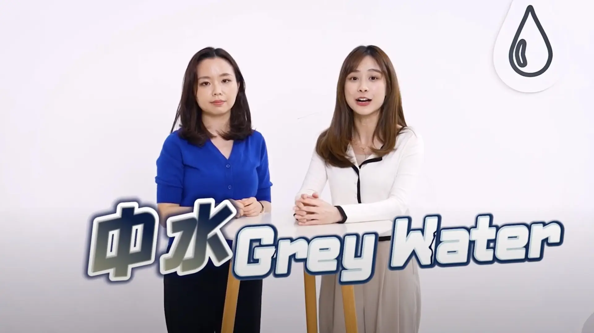 Two women stand next to each other against a plain white background. The woman on the left wears a blue shirt, while the woman on the right dons a white top. The text "Grey Water" appears prominently in front of them with a water drop icon, as part of a promotional video.