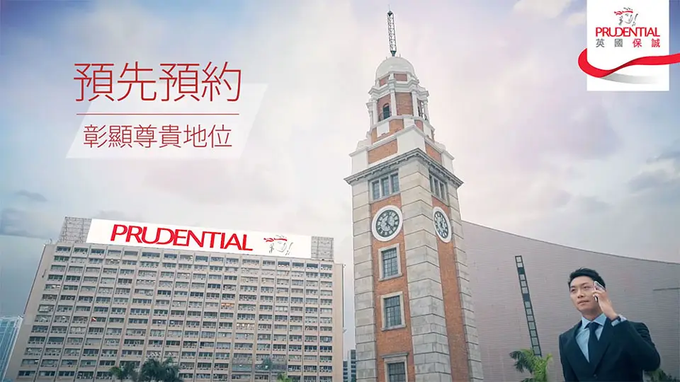 A professionally dressed man talks on his smartphone in front of a large historic clock tower and adjacent building. The Prudential logo and Chinese text are displayed prominently on the image, promoting a service. It could be part of an engaging construction video that highlights prominent landmarks.