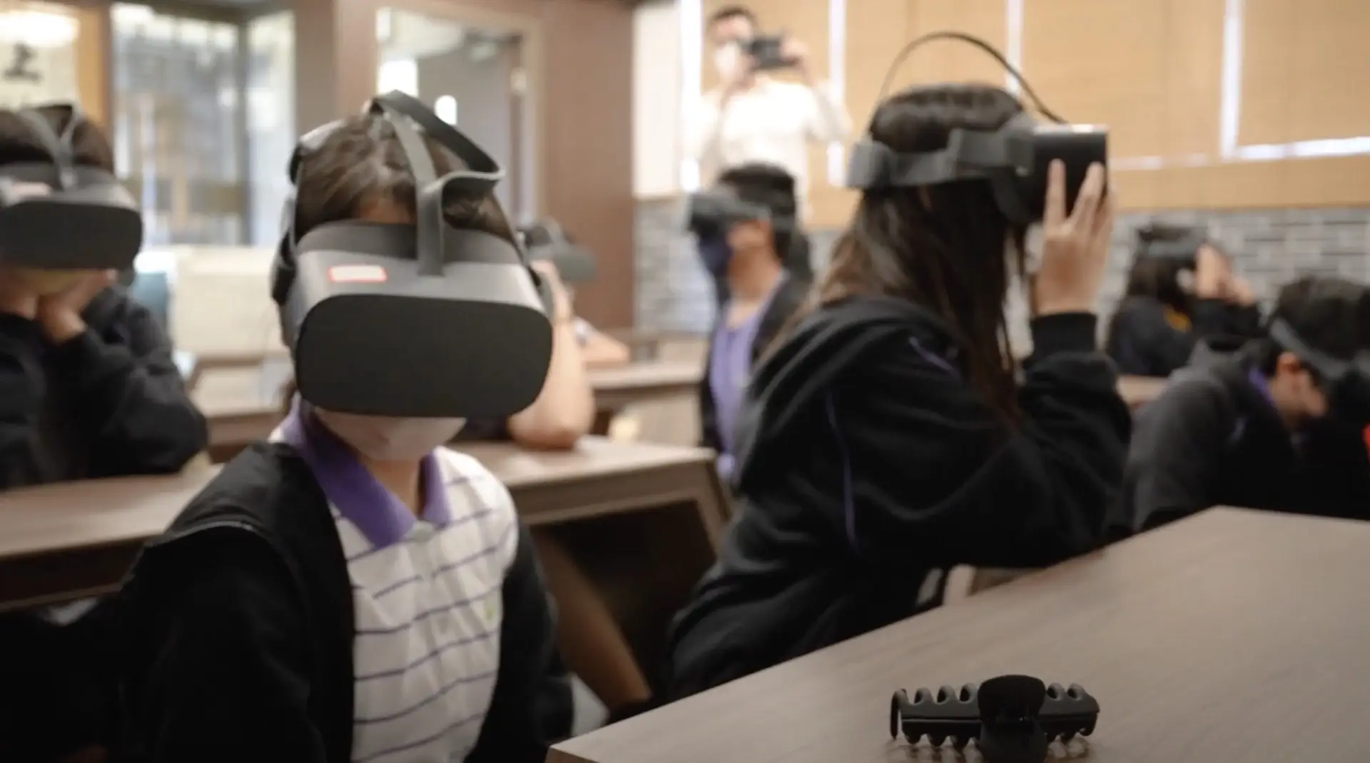 Students seated in a classroom wear virtual reality headsets, engaging with VR content. They are focused, and the room is equipped with desks and other educational materials. The experience feels like an immersive exhibition promotion.