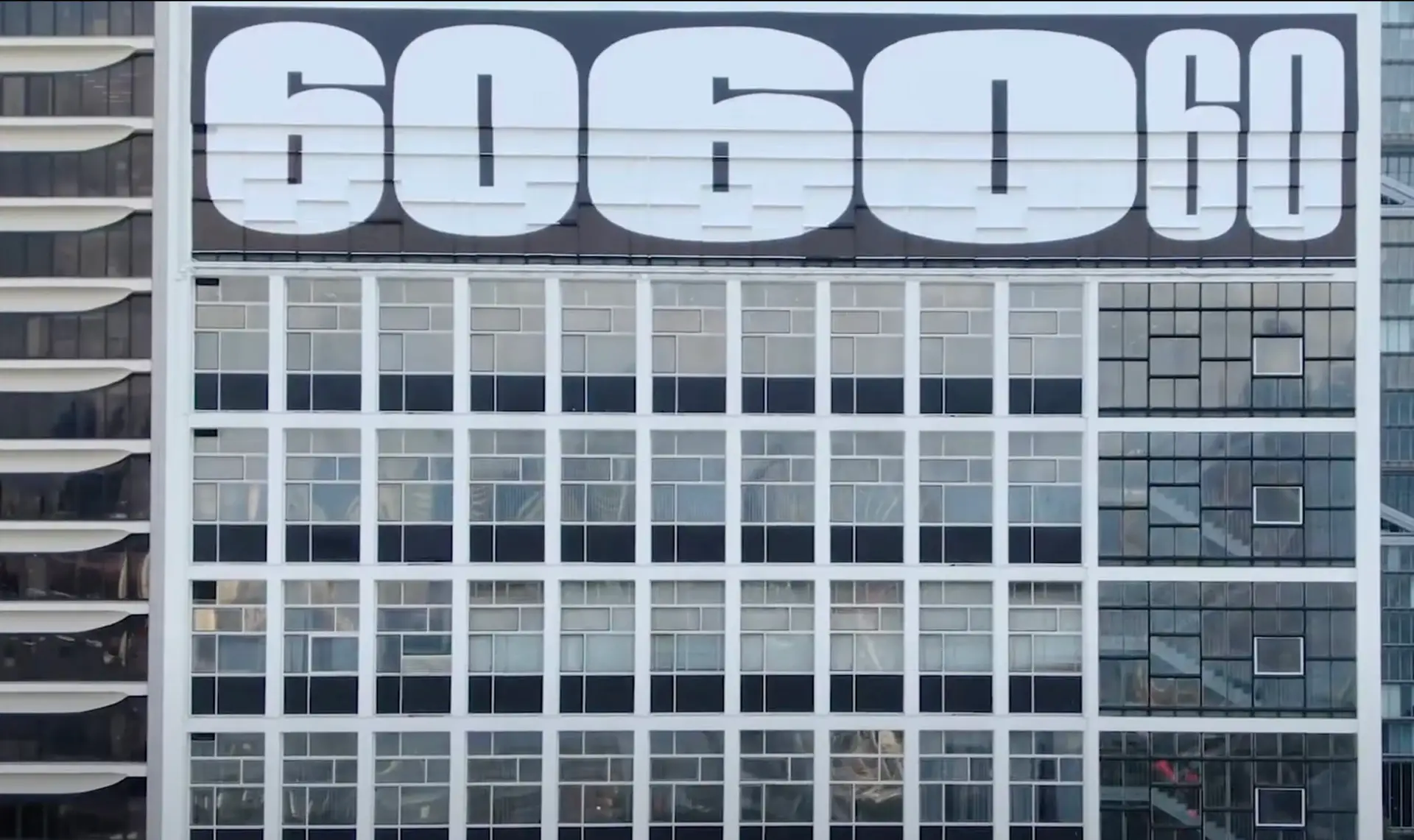 An office building exterior with large numerals "6060" displayed prominently at the top. The building facade showcases a grid of large windows, reflecting the sky and surroundings. Modern architectural design elements make it ideal for promotional video shoots highlighting urban advancements.