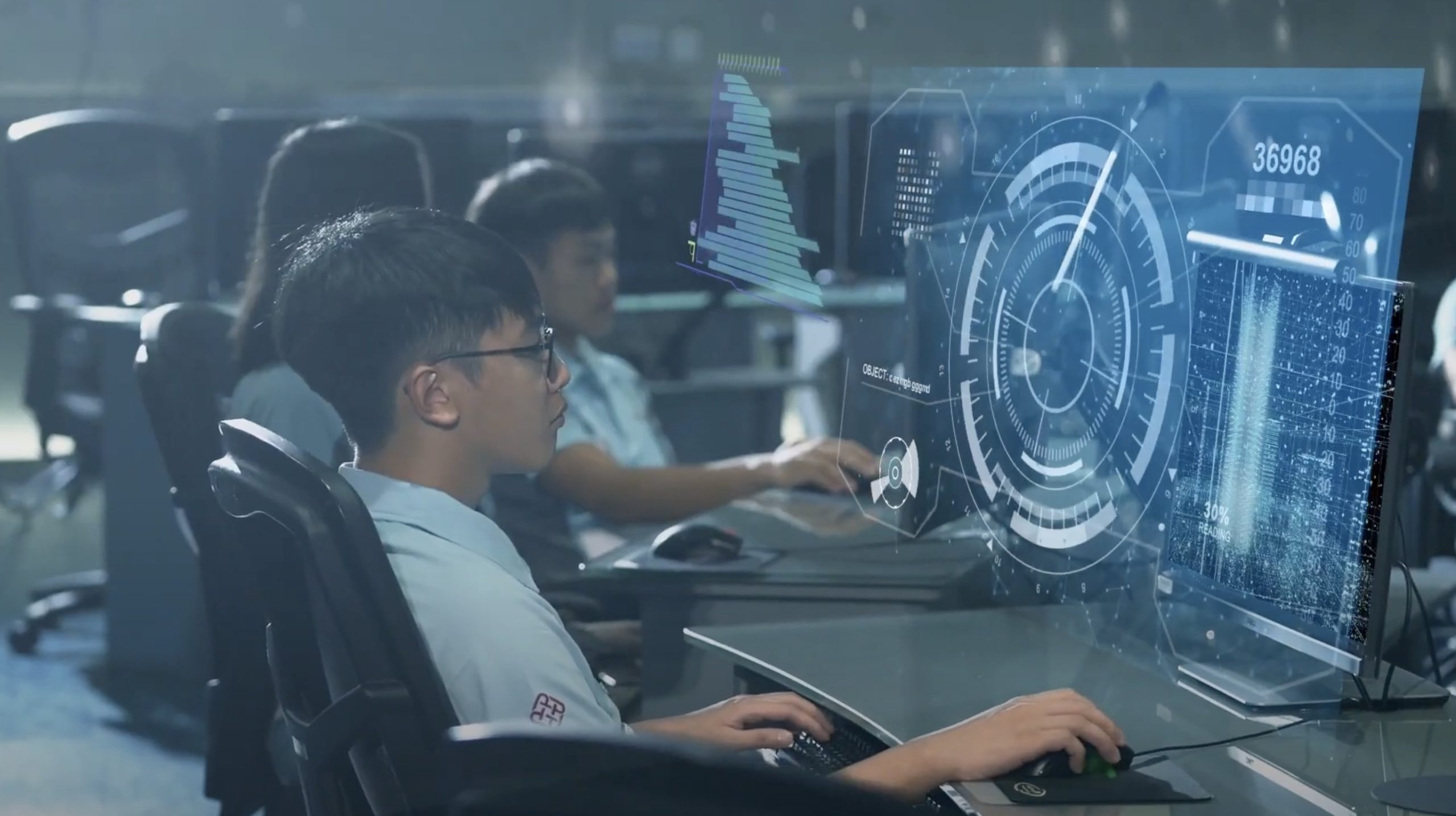 A young person sits at a desk using a computer with futuristic digital graphics and data visualizations projected on the screen. Other students work at computers in the background. The setting appears to be a modern classroom or lab.