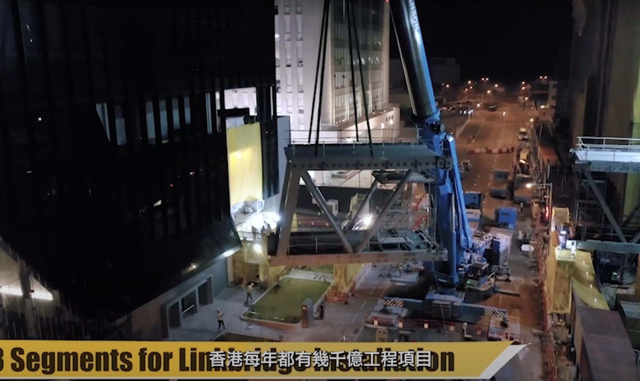 A nighttime construction scene shows a large crane lifting a steel structure between buildings on a city street. Workers and vehicles are visible below. Partial English and Chinese text appears at the bottom.