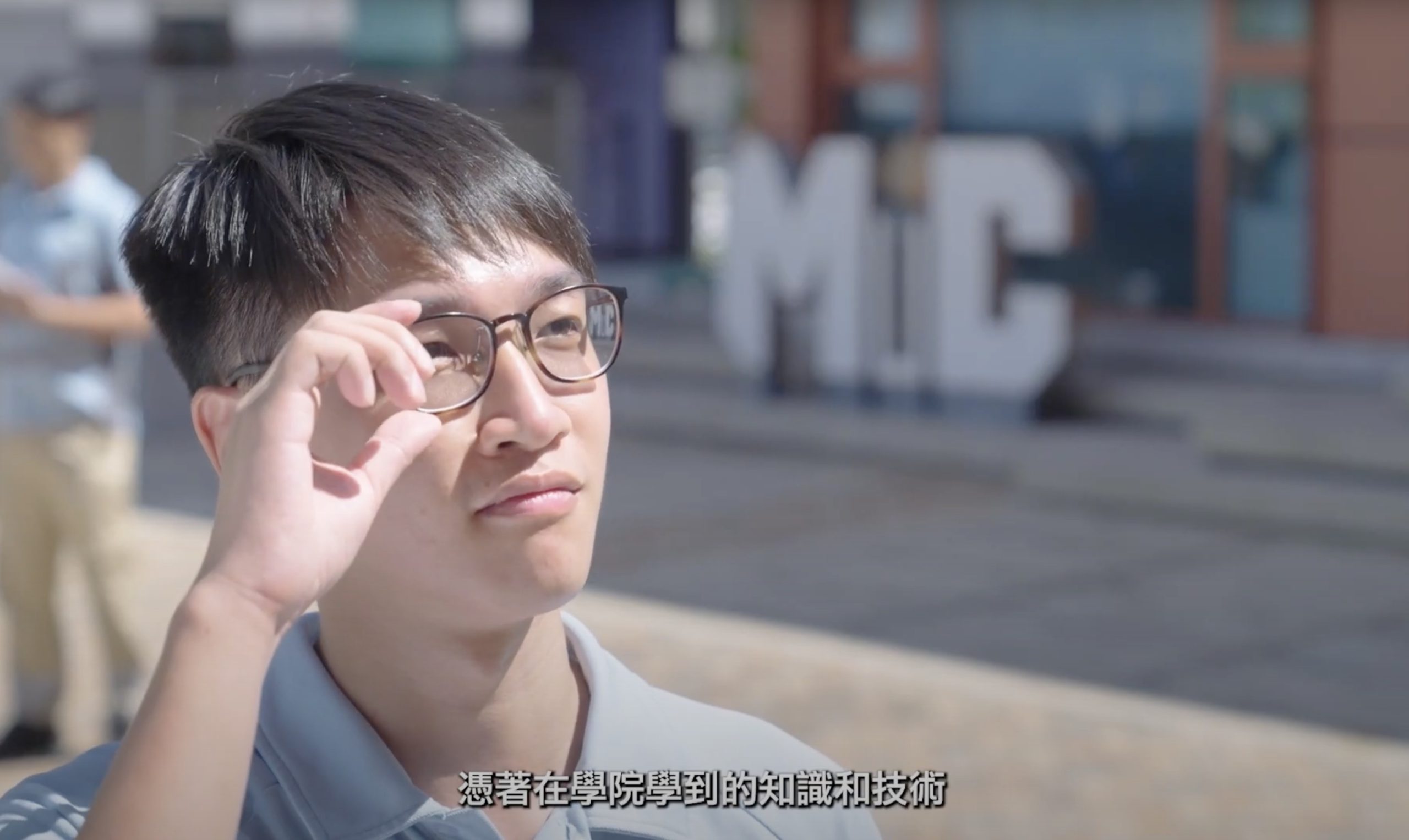 A young person adjusts their glasses outdoors, with blurred large white "MC" letters in the background. Chinese text appears at the bottom of the image.