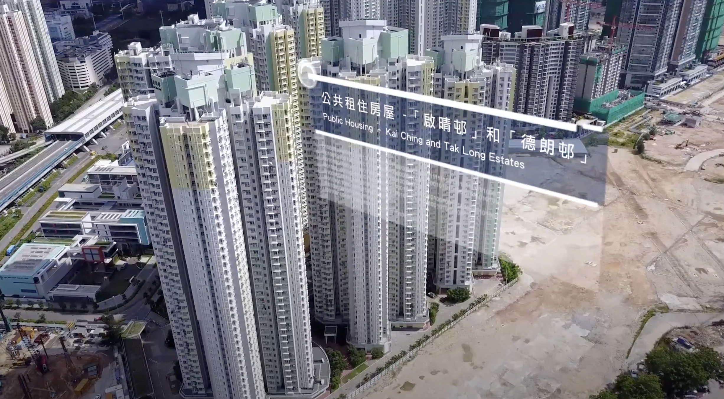 Aerial view of tall residential apartment buildings labeled "Public Housing, Kai Ching and Tak Long Estates" in English and Chinese, with a large empty lot beside the buildings.