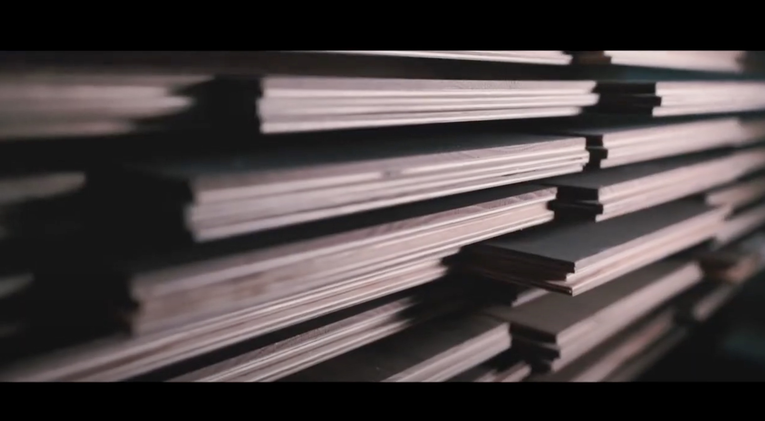 A close-up of several stacks of plywood sheets arranged in a horizontal pile, with soft lighting highlighting the layered edges and creating a sense of depth.