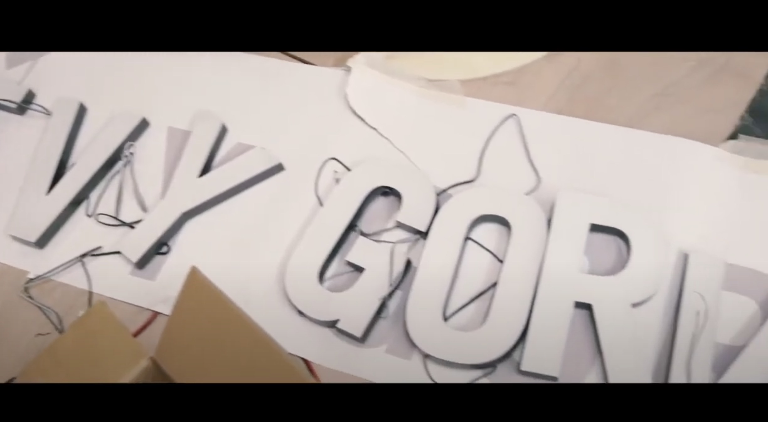 Large white letters with black edges spelling "VY GOR" are lying on a white surface, surrounded by wires and cardboard. The letters appear to be part of a sign being assembled or repaired.