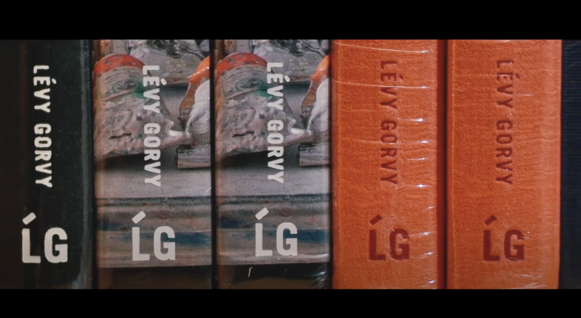 Close-up of five books standing upright. Three have colorful abstract covers, and two are solid orange. All spines display the publisher's name "LÉVY GORVY" and the initials "LG" in white, with the orange books wrapped in plastic.