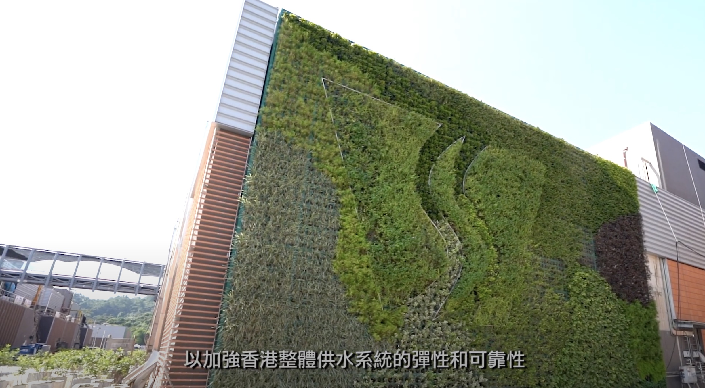 A modern building with a large vertical green wall covered in various plants and a stylized leaf design. Chinese text at the bottom overlays the image.