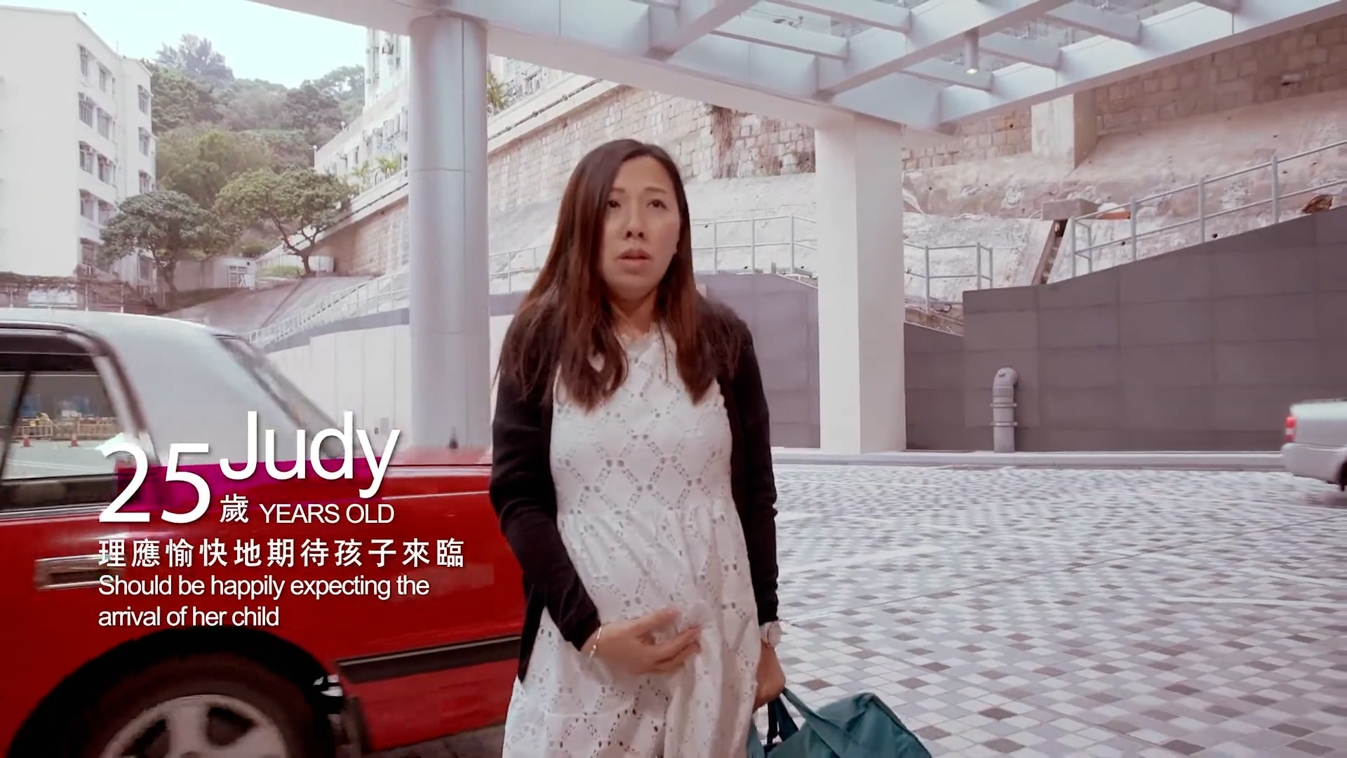 A pregnant woman stands outdoors near a red car, holding her belly with one hand and a green bag in the other. Text on the image reads, "25 Judy, 25 YEARS OLD, Should be happily expecting the arrival of her child.