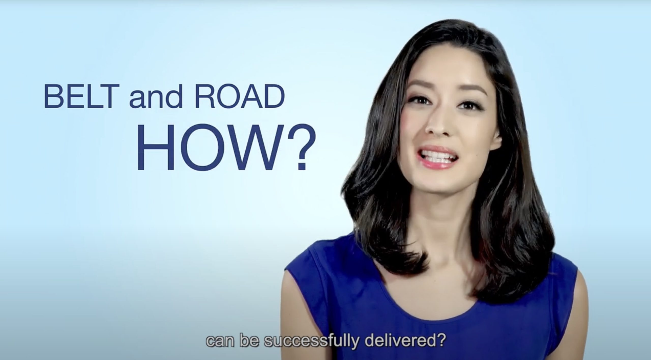 A woman with dark hair wearing a blue top speaks in front of text that reads "BELT and ROAD HOW?" on a light blue background. Subtitles at the bottom say, "can be successfully delivered?.