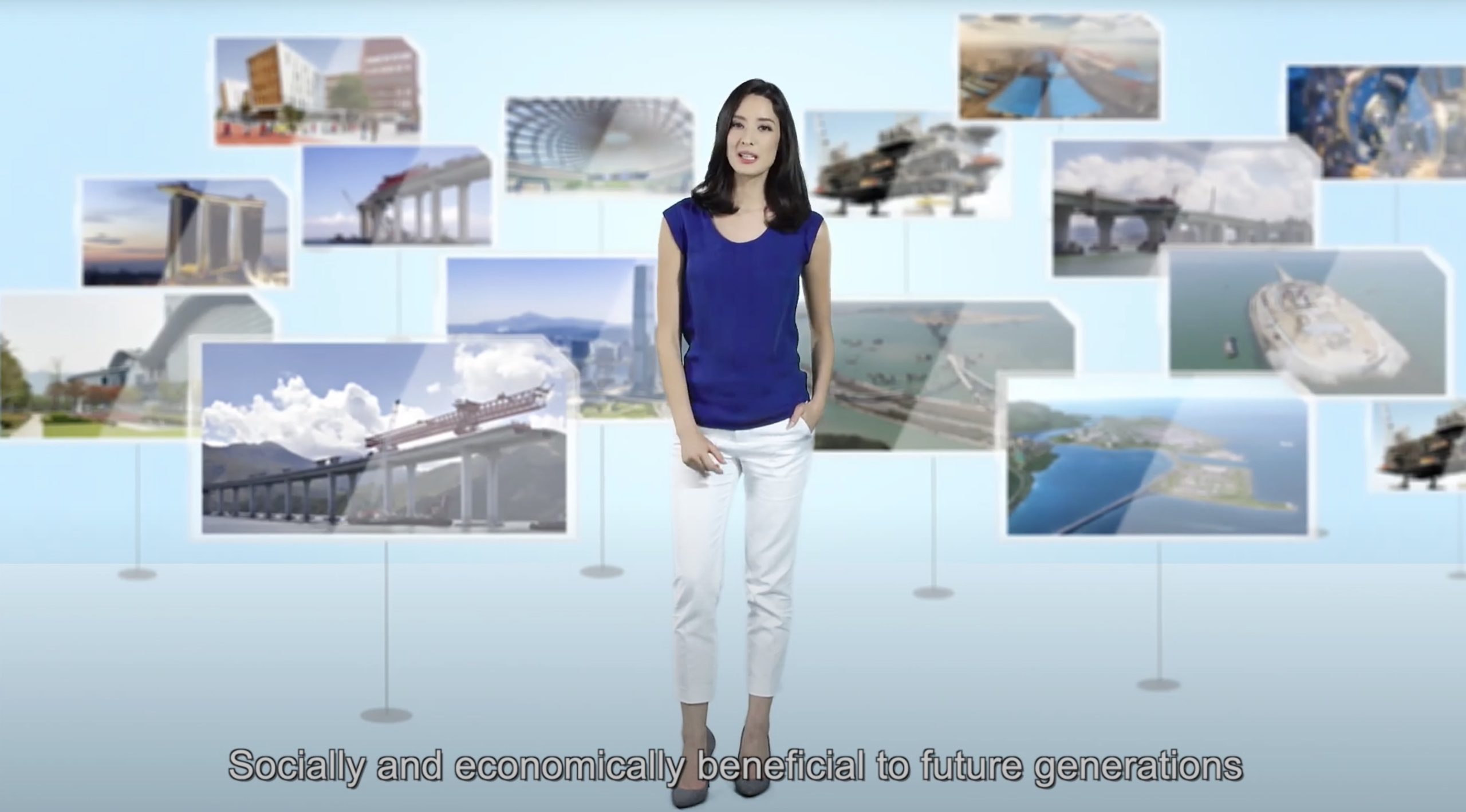 A woman in a blue top and white pants stands in front of a backdrop displaying various infrastructure and cityscape images. Subtitle reads: "Socially and economically beneficial to future generations.