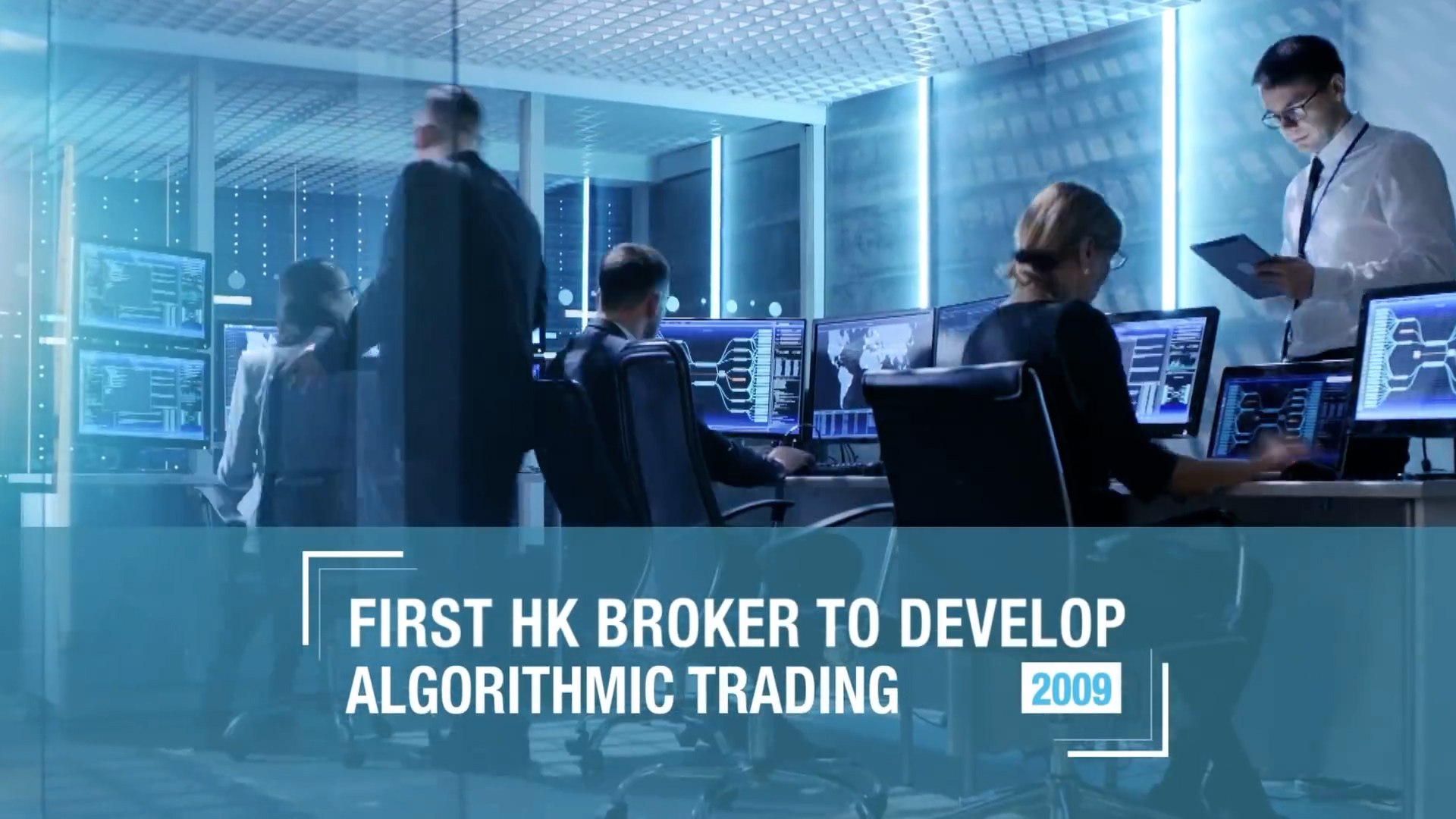 People in business attire work at computers in a modern, glass-walled office. Text overlay reads, "First HK broker to develop algorithmic trading 2009." The scene suggests a high-tech financial environment.
