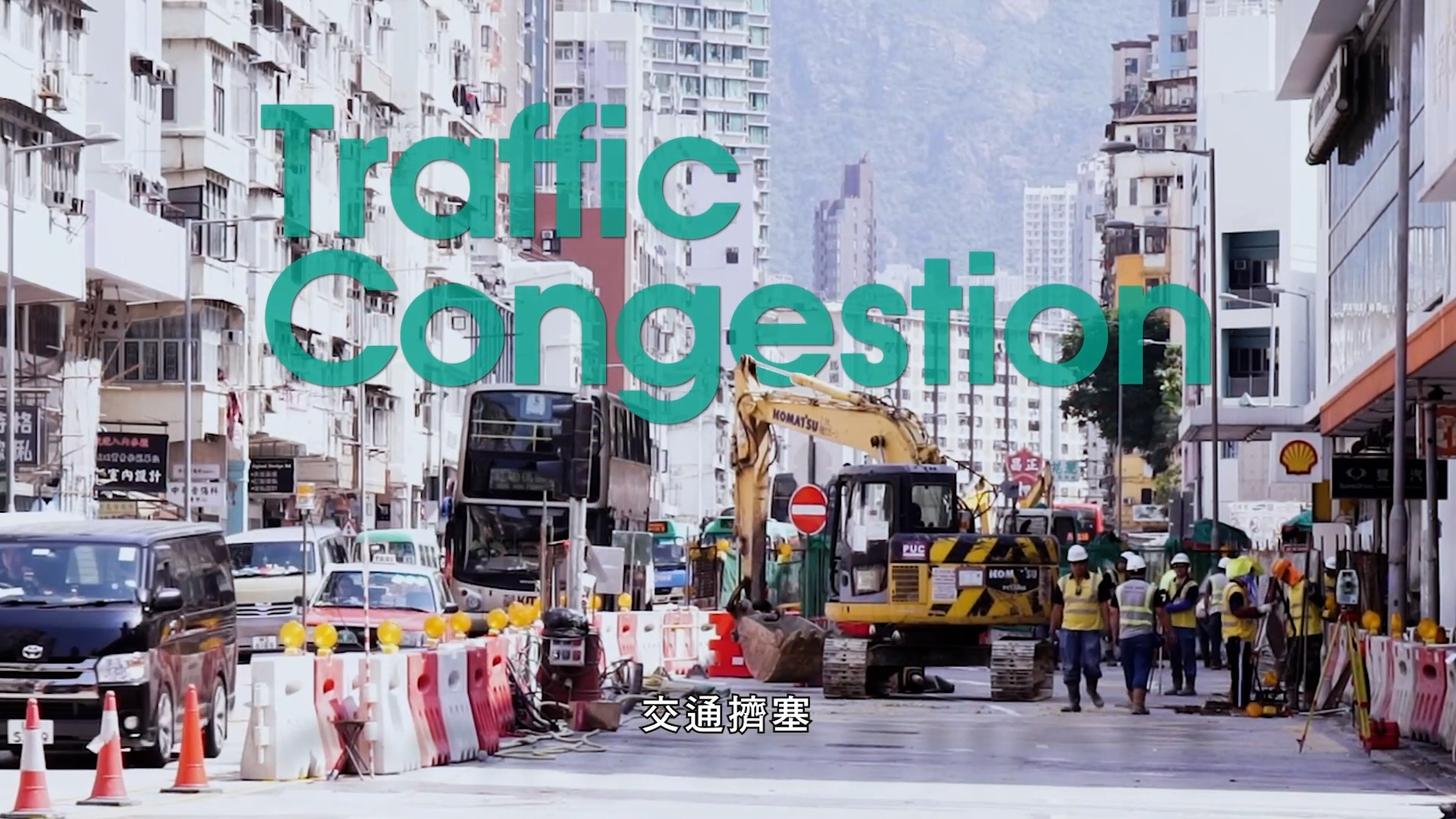 A busy city street with construction vehicles, workers, traffic barriers, and double-decker buses. Large text reads "Traffic Congestion" and there are Chinese subtitles at the bottom. Tall buildings line both sides.