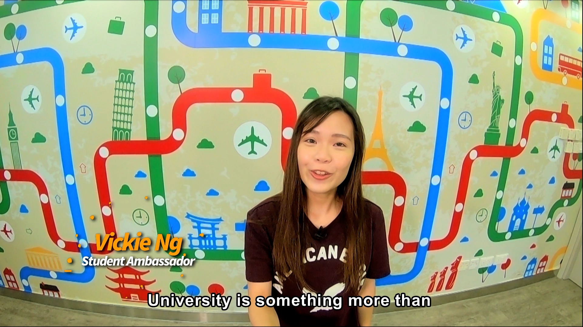A young woman stands in front of a colorful, travel-themed wall with transport icons and landmarks. Text on the image reads, "Vickie Ng, Student Ambassador." Subtitles say, "University is something more than.