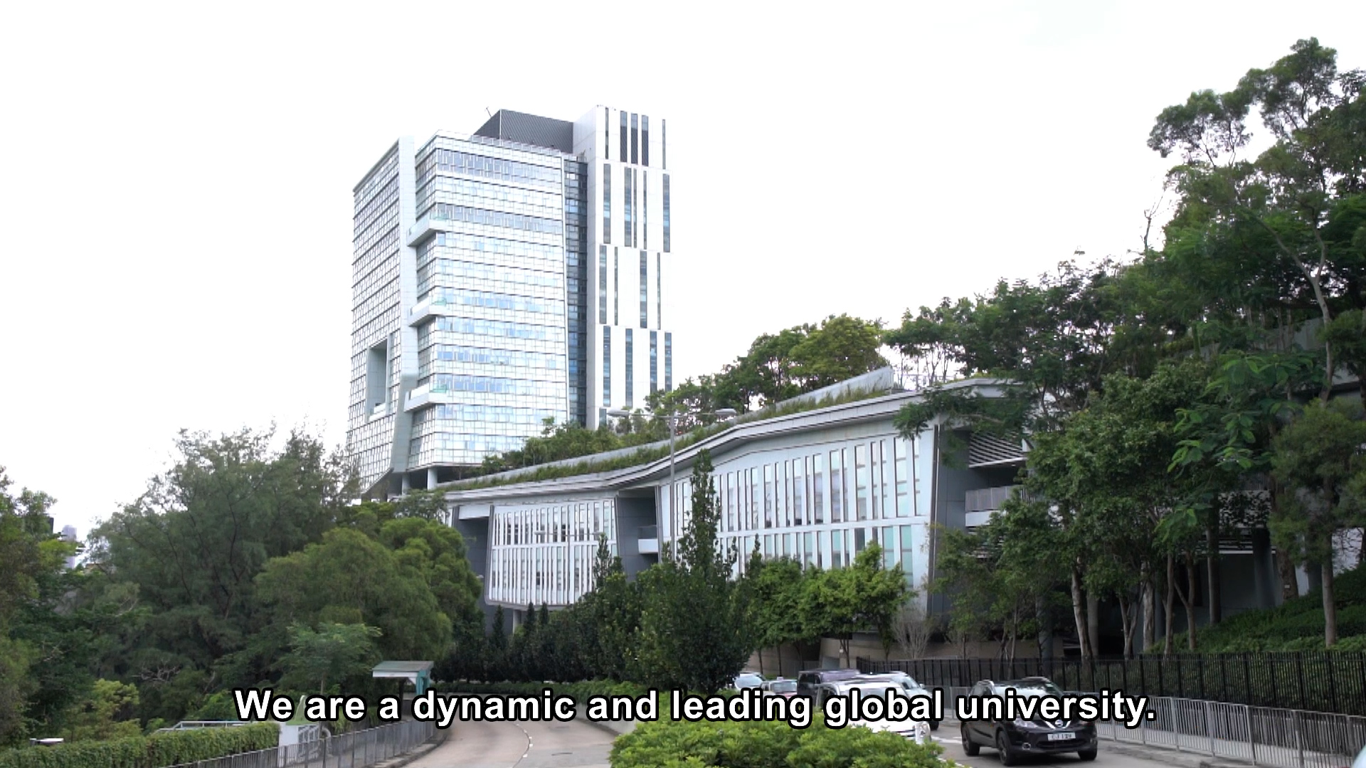 A modern university campus with tall glass buildings surrounded by trees; a caption at the bottom reads, "We are a dynamic and leading global university.