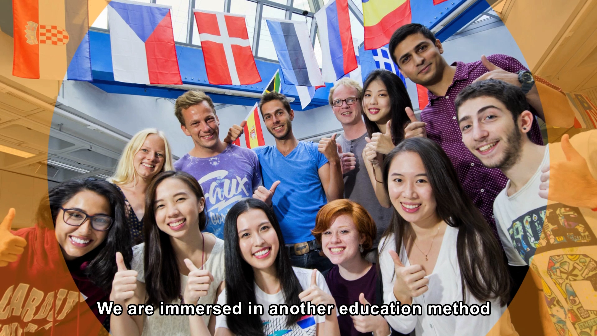 A diverse group of smiling young adults stand indoors, giving thumbs-up, with international flags hanging above them. Text at the bottom reads, "We are immersed in another education method.