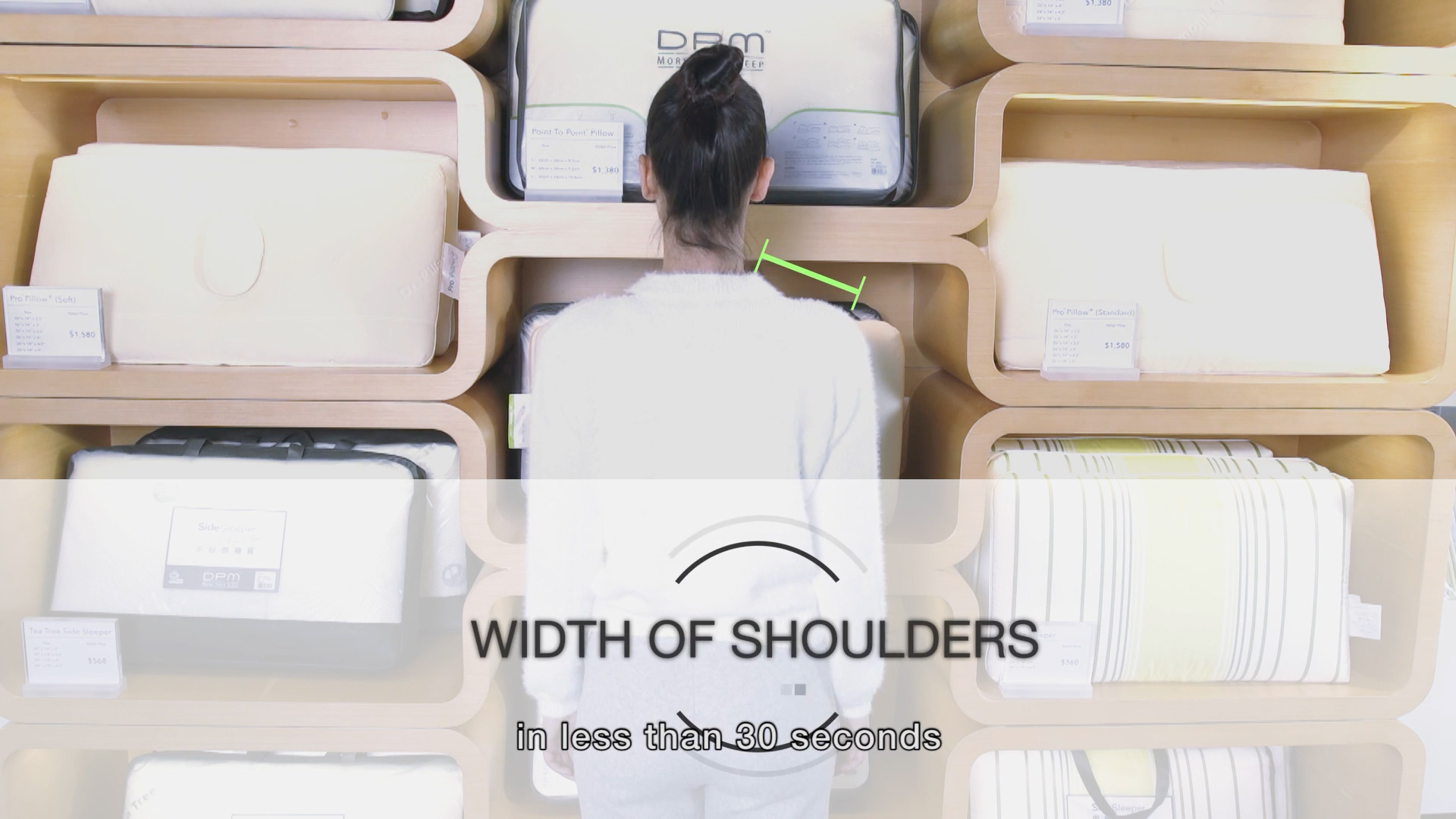 A person with dark hair in a bun stands with their back to the camera against a wooden shelving display, as a graphic measures the width of their shoulders. Text reads: "WIDTH OF SHOULDERS in less than 30 seconds.