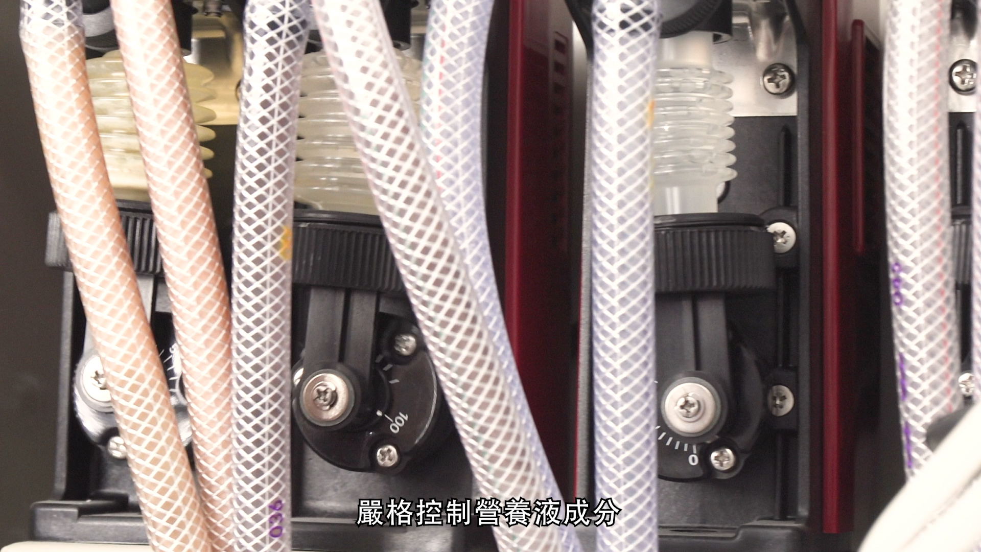 Close-up of a machine with tubes and control knobs, likely used for handling liquids. There are transparent and white braided tubes connected, and Chinese text appears at the bottom of the image.