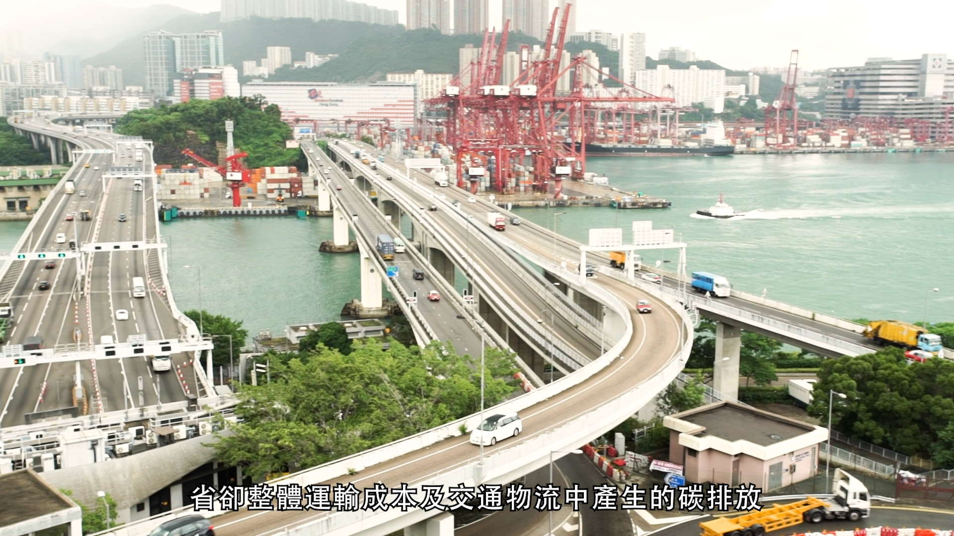 Aerial view of highways with vehicles and trucks near a busy port with shipping containers, cranes, and city buildings in the background; Chinese text is overlaid at the bottom.