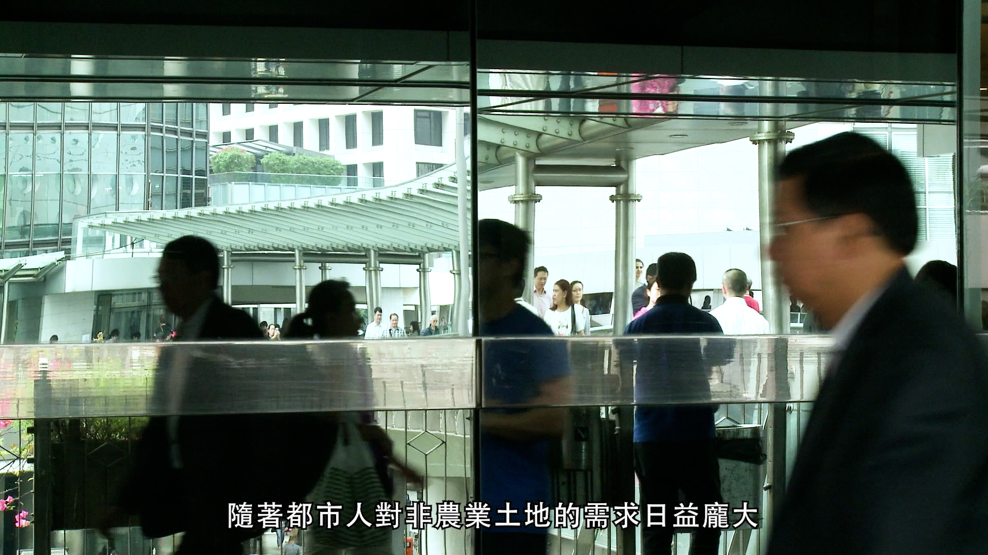 People walking past a glass building with reflections of city life; Chinese text is overlaid at the bottom of the image.