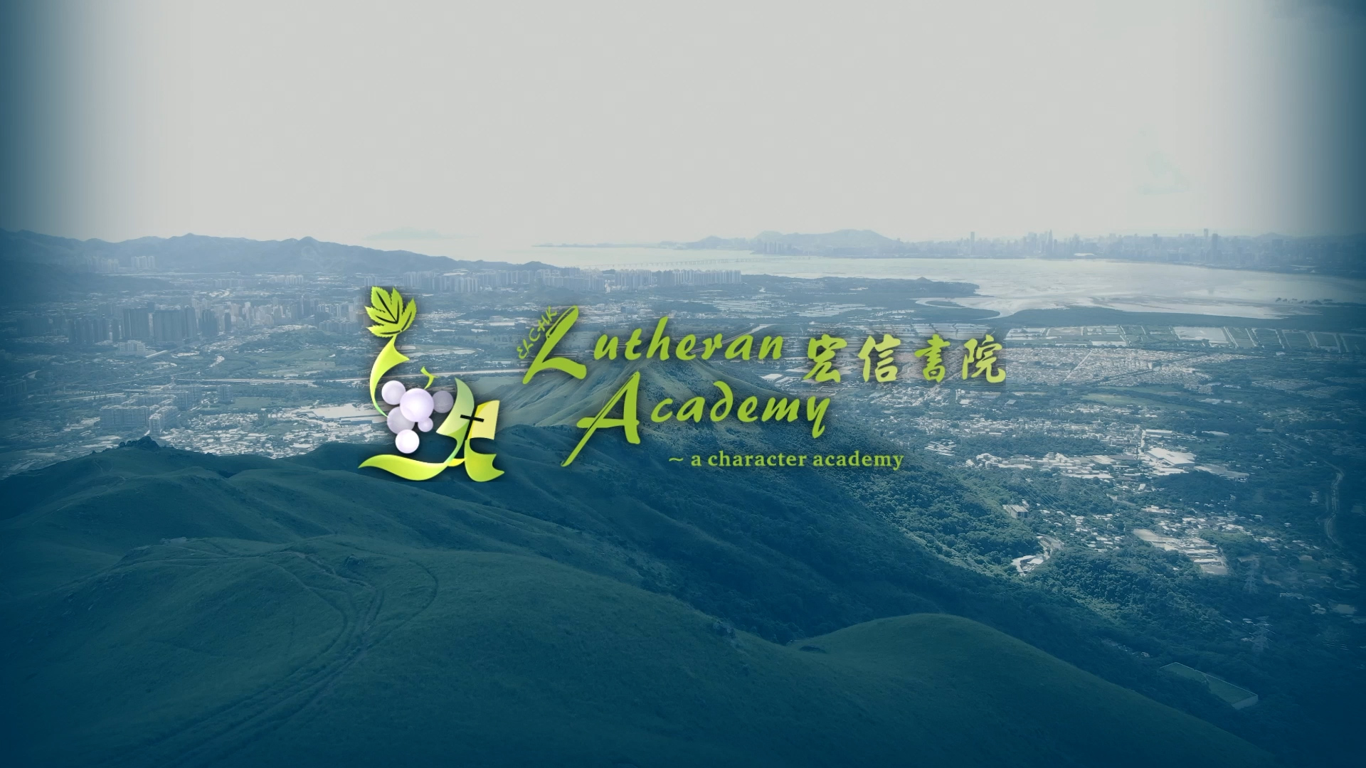 Aerial view of green hills and a cityscape in the distance, overlaid with the Lutheran Academy logo and the text “a character academy” in yellow and green, along with grapes and leaf graphics.