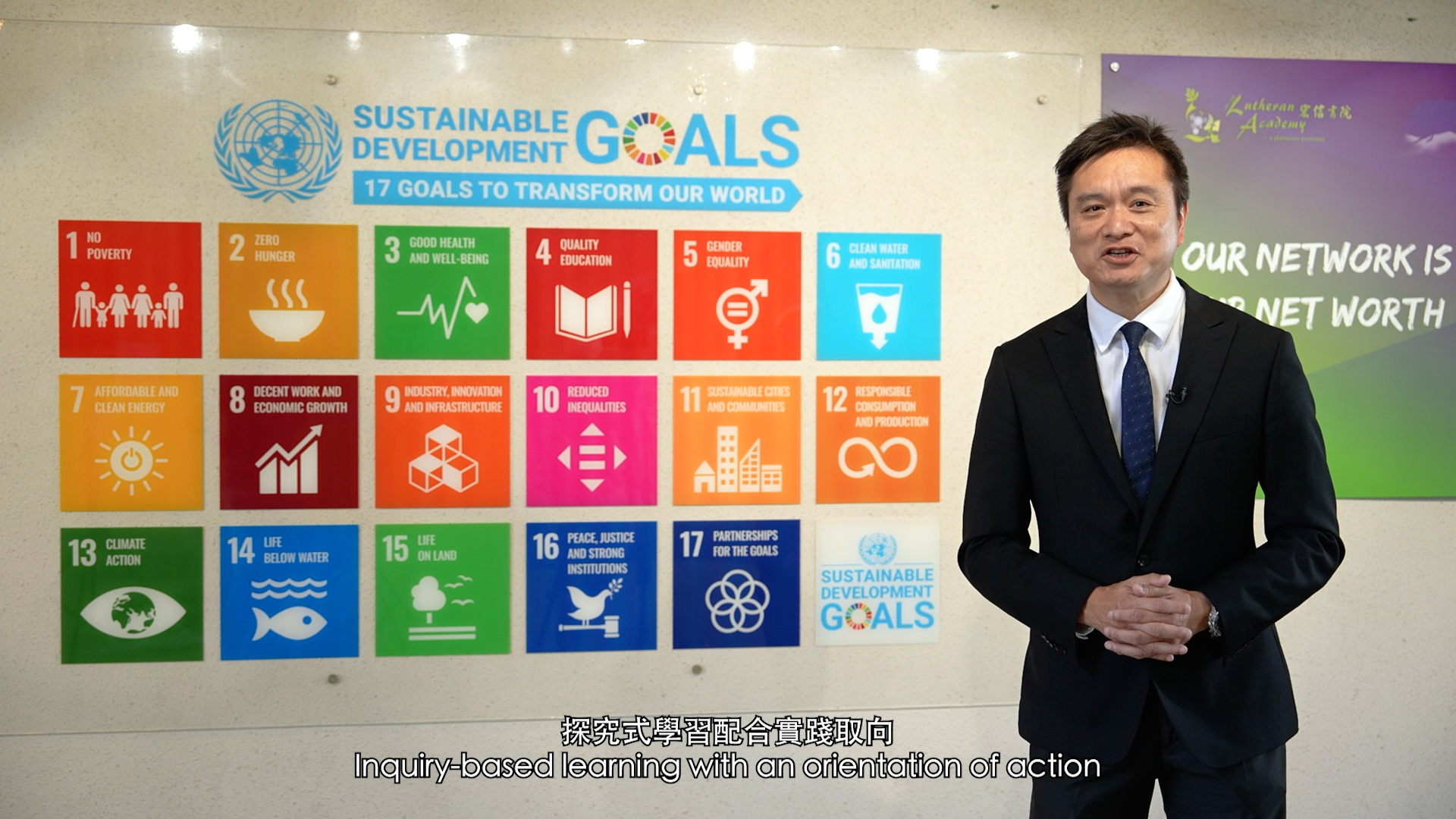 A man in a suit stands indoors next to a colorful display of the UN’s 17 Sustainable Development Goals. Text at the bottom reads: "Inquiry-based learning with an orientation of action.