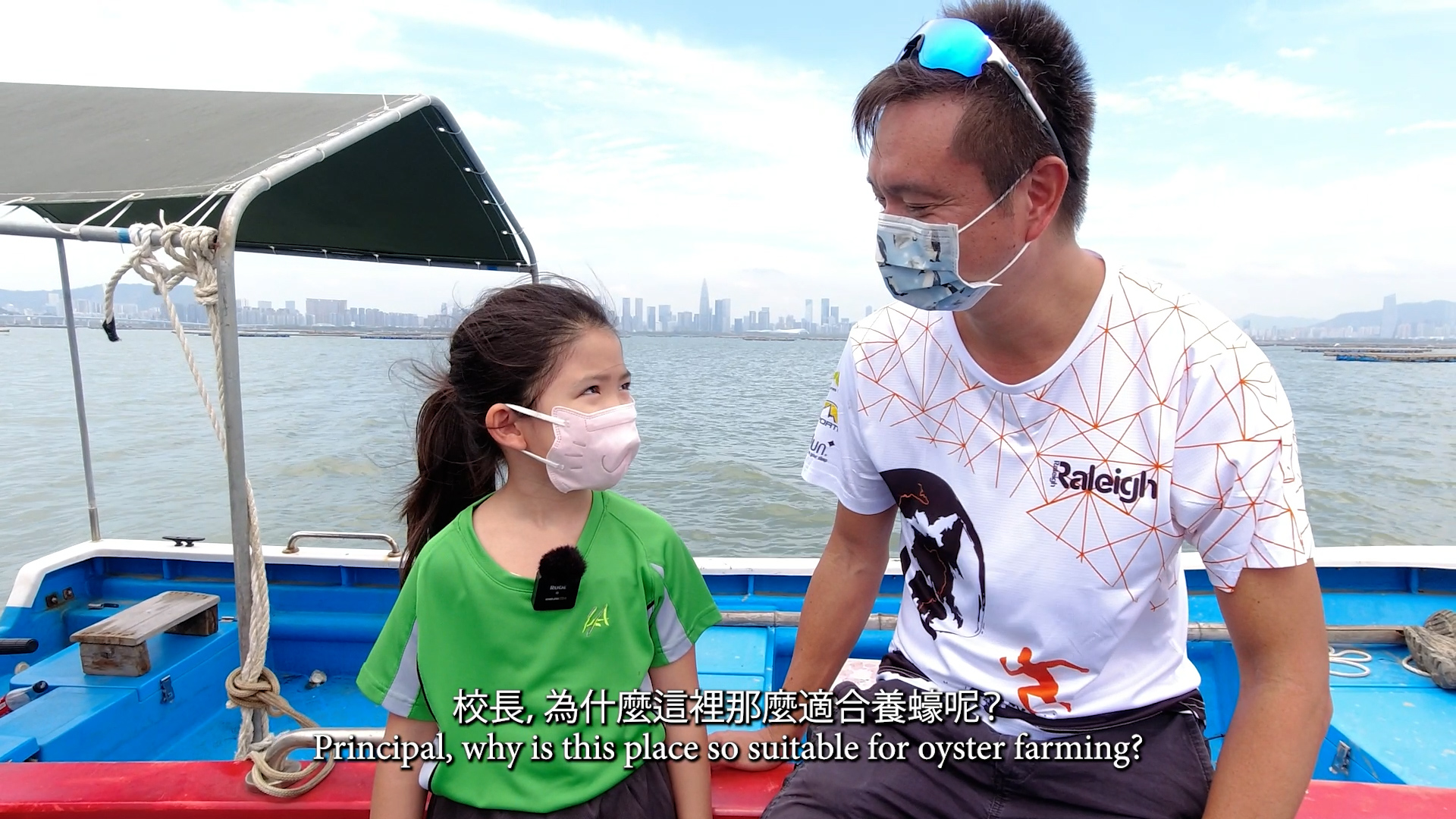 A young girl and a man sit on a blue and red boat, both wearing face masks. They talk and smile at each other, with water and a city skyline in the background. Chinese and English subtitles are displayed at the bottom.
