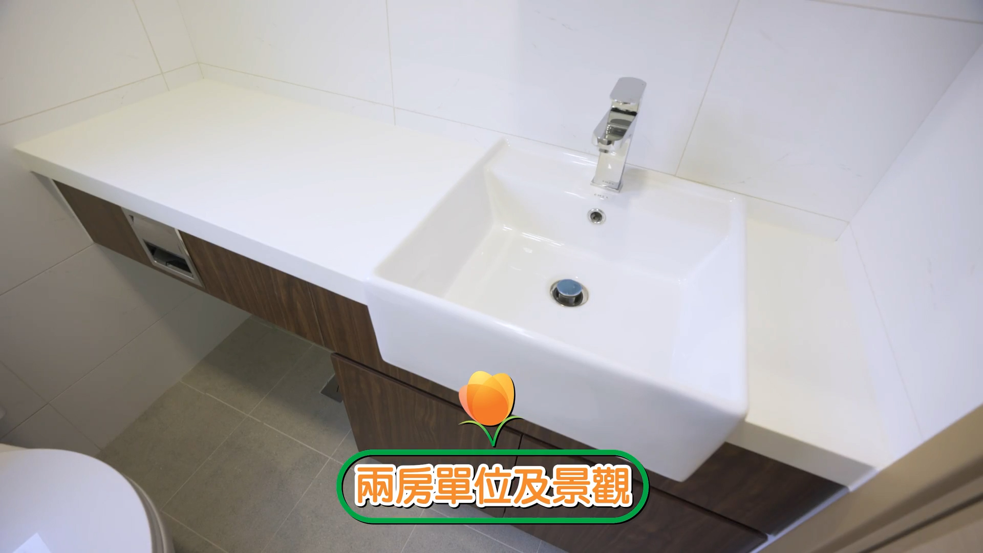 A modern white bathroom sink with a chrome faucet, set in a countertop with wooden cabinets below. There is Chinese text with an orange flower icon at the bottom of the image.