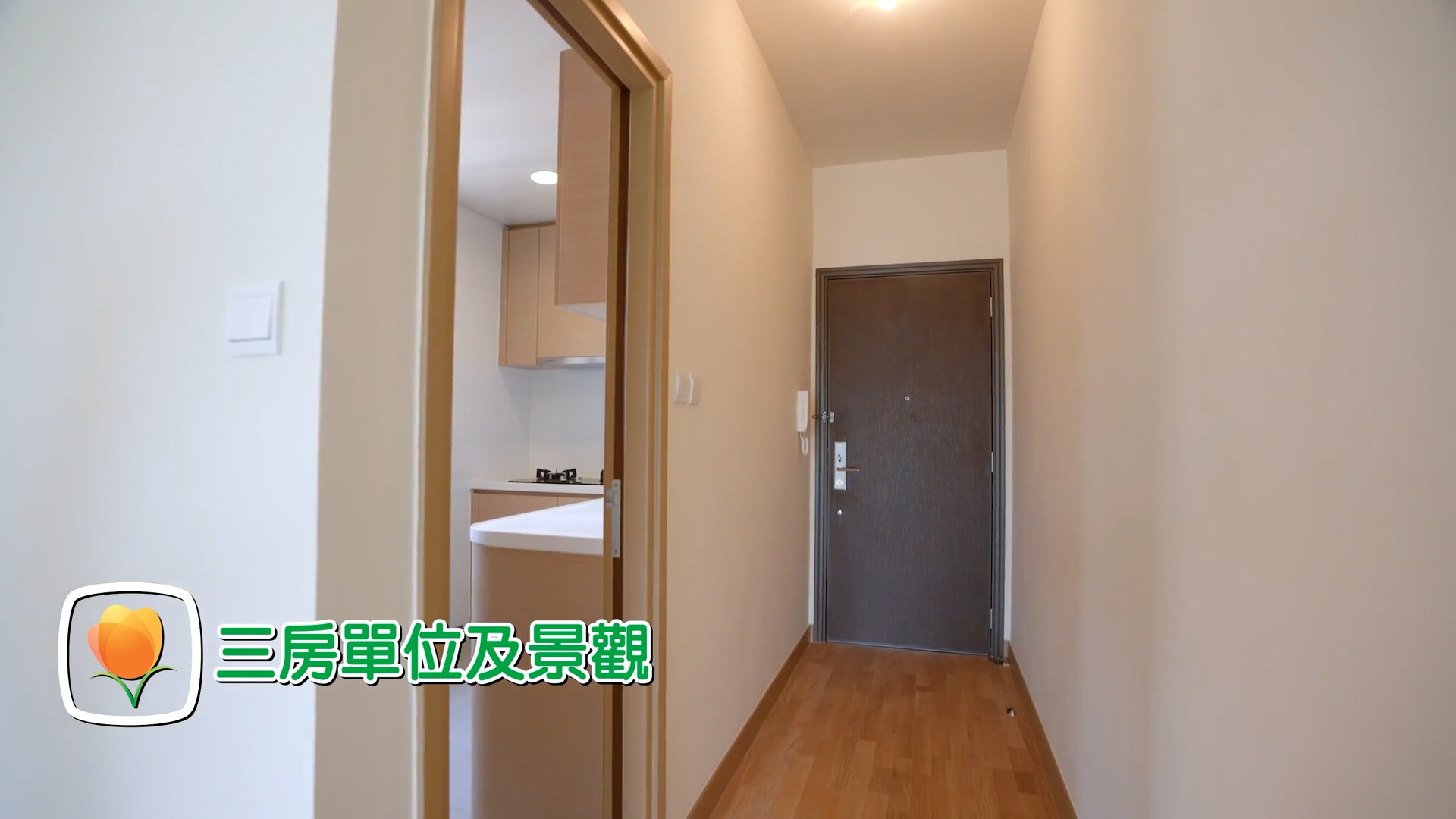 A hallway in an apartment with light-colored walls and wooden flooring, leading to a closed door. A kitchen area is partially visible through an open door. Chinese text and a flower icon are overlaid in the bottom left corner.
