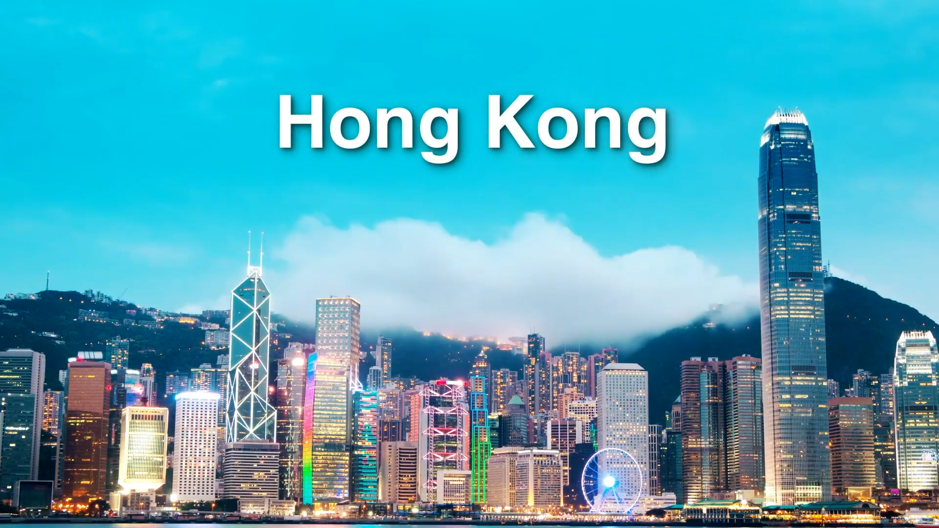 Hong Kong skyline with tall modern skyscrapers under a bright blue sky, clouds over the mountains in the background, and “Hong Kong” written in bold white letters at the top.
