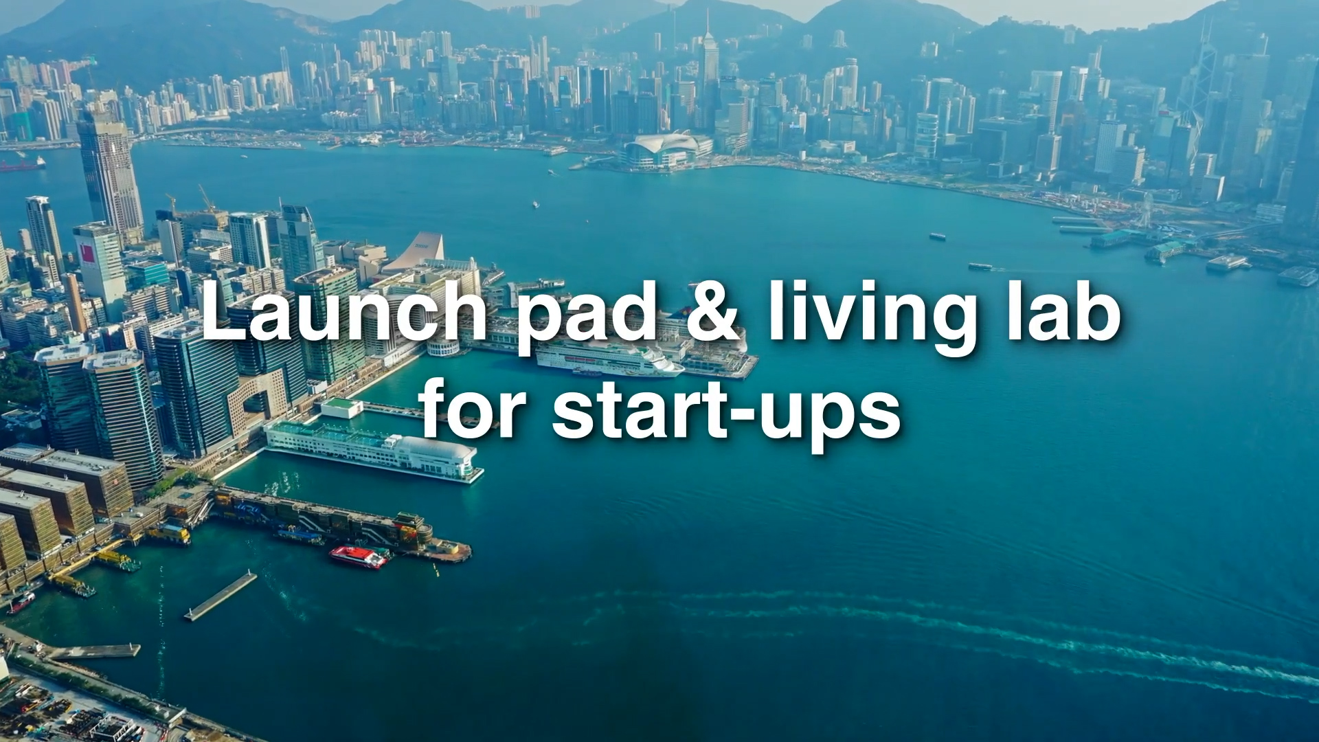 Aerial view of a coastal city with tall buildings and a harbor. White text over the water reads: "Launch pad & living lab for start-ups.