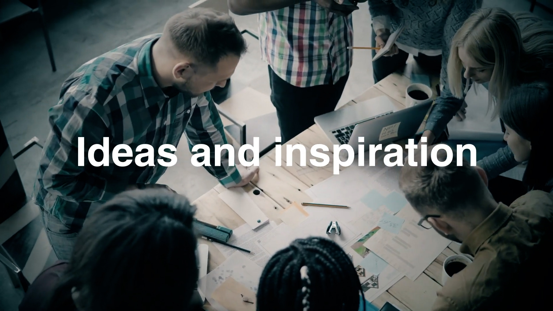 A group of people collaborate around a table covered with papers, notebooks, and laptops. The text "Ideas and inspiration" is displayed across the center of the image.