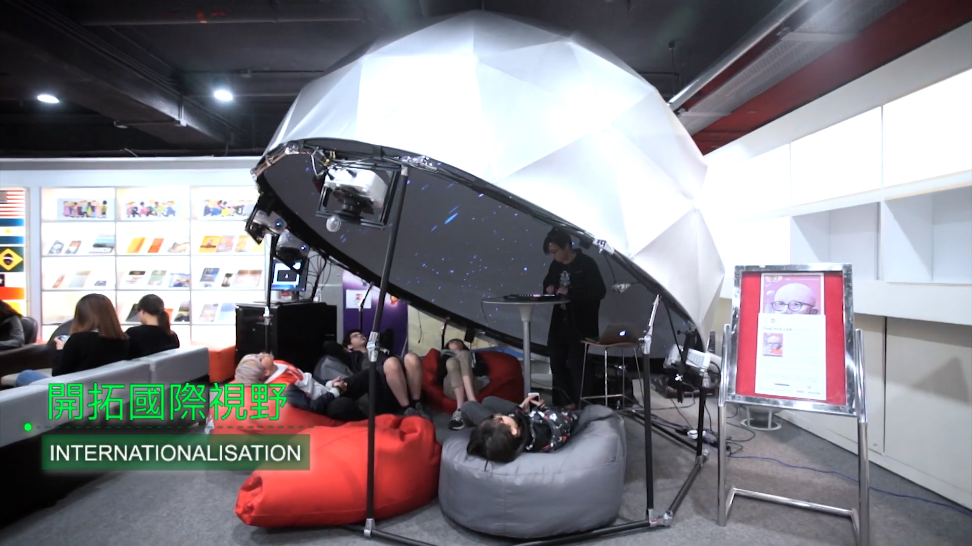 People are relaxing on bean bags inside a dome-shaped structure with a starry ceiling, inside a modern library or learning space. A person is operating equipment nearby. A sign reads "INTERNATIONALISATION" in English and Chinese.