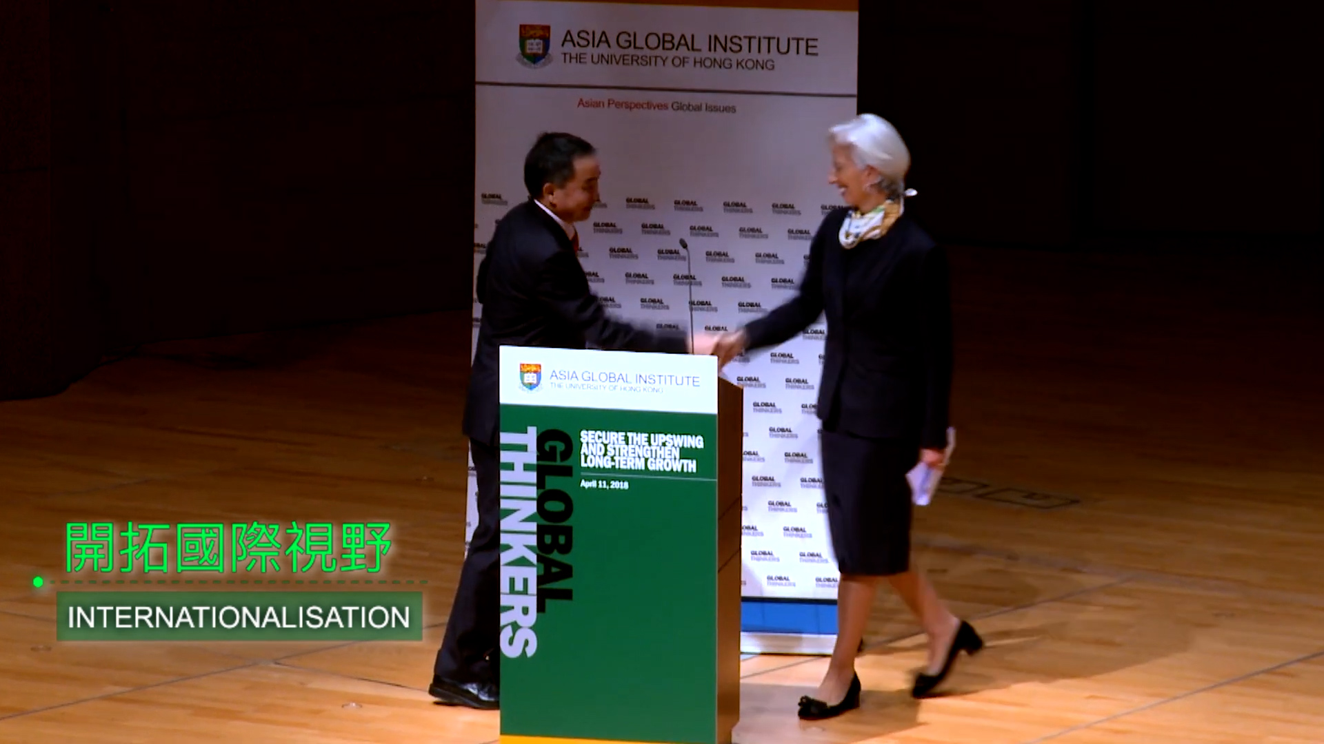 A man and a woman shake hands on stage at an Asia Global Institute event. They stand beside a podium labeled "GLOBAL THINKERS" and a background banner from The University of Hong Kong. Text overlay reads "INTERNATIONALISATION.