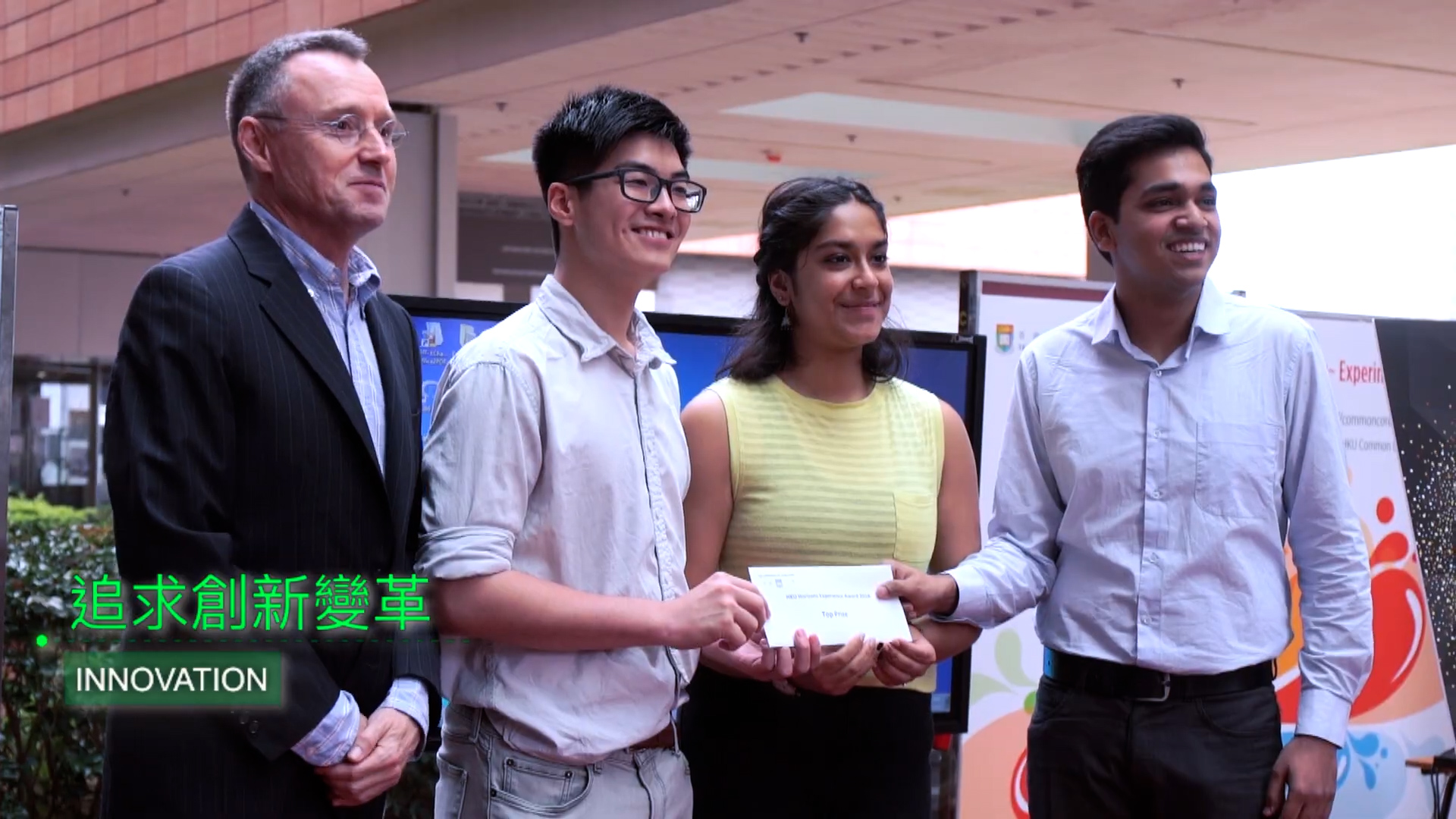 Four people stand together smiling; one is holding an envelope. They are outdoors near a modern building. The text "INNOVATION" and Chinese characters appear in the lower left corner.