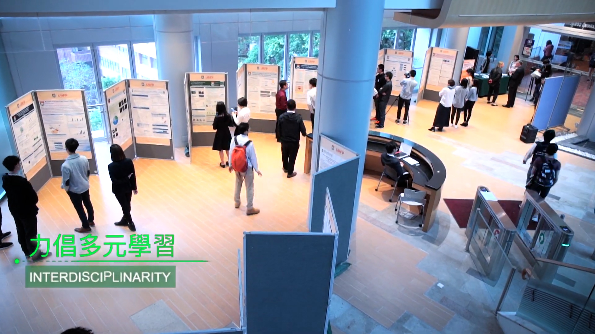 People stand and look at research posters displayed on boards in a spacious, modern hall with large windows and pillars. Text in Chinese and English reads “Interdisciplinarity.”.