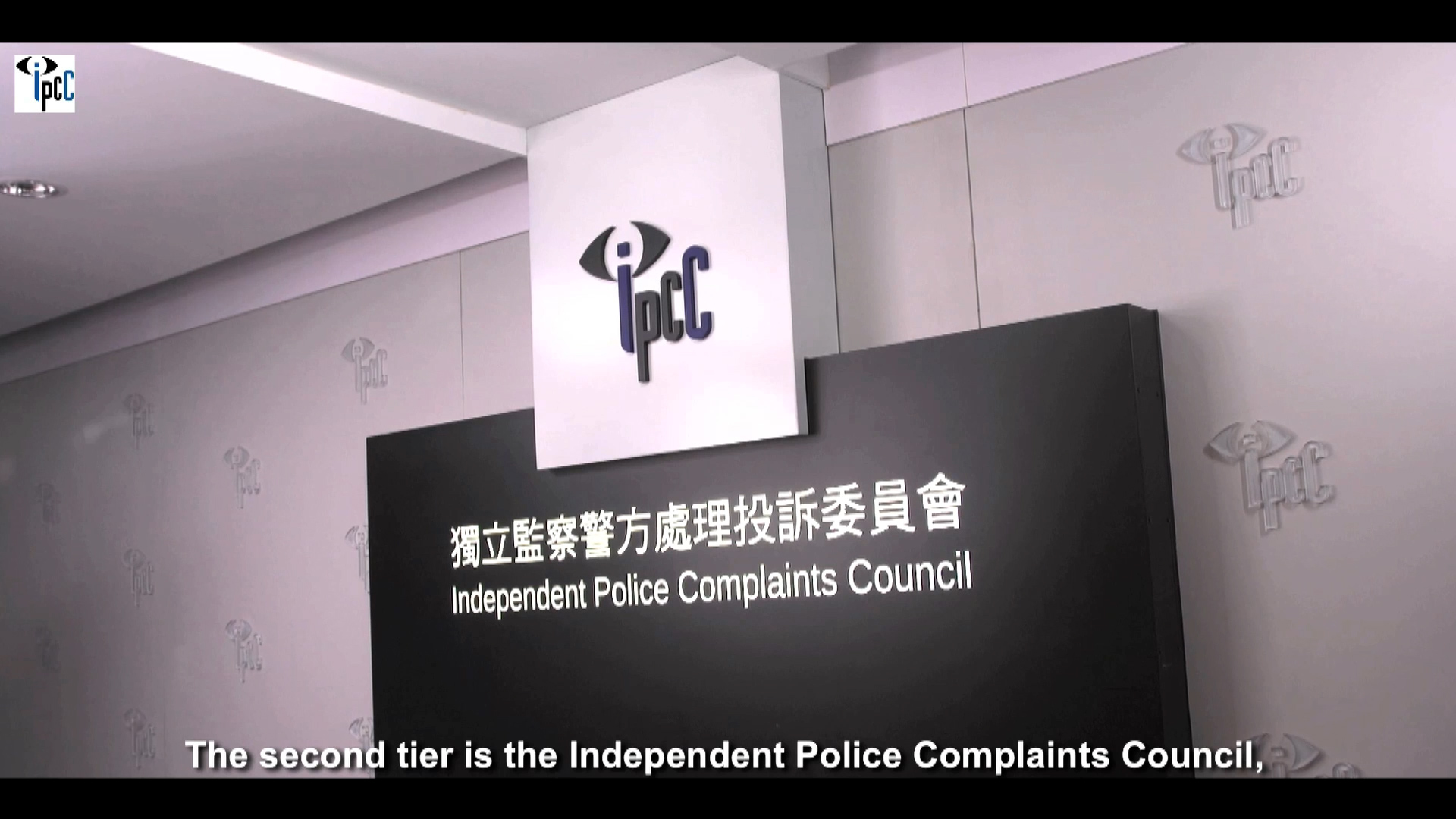 A sign on a wall displays the logo and name of the Independent Police Complaints Council in both Chinese and English. Subtitles at the bottom read, "The second tier is the Independent Police Complaints Council.