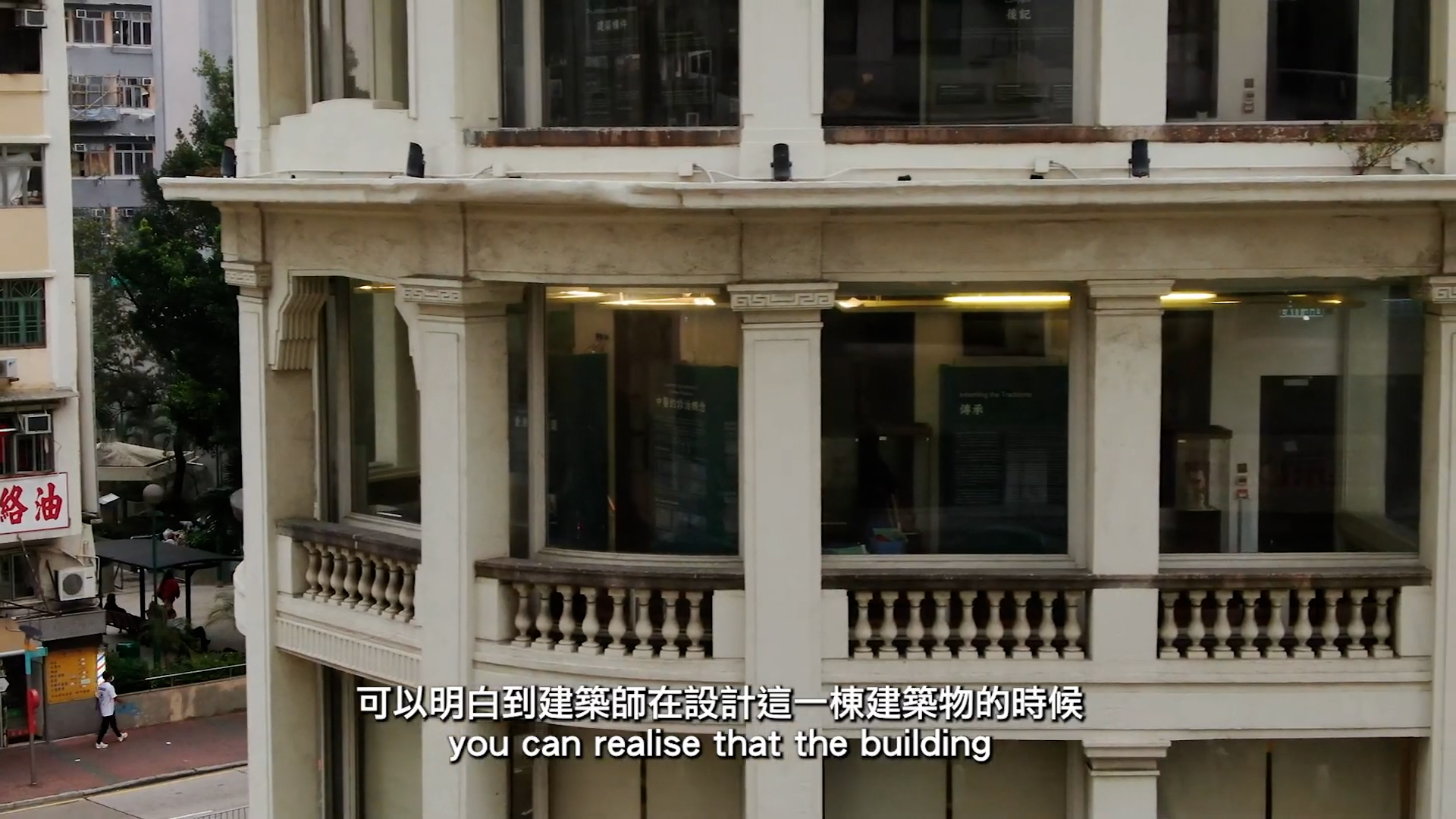 A close-up of the exterior of a white, historic building with columns and large windows. Subtitles at the bottom read: "you can realise that the building." Chinese text is also visible above the subtitles.