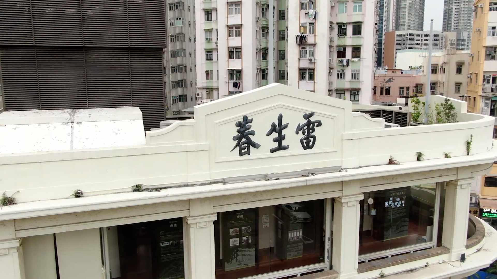 A white building with large Chinese characters on the facade, set against a backdrop of tall, closely packed apartment buildings in an urban area. The building has large windows and classical architectural details.