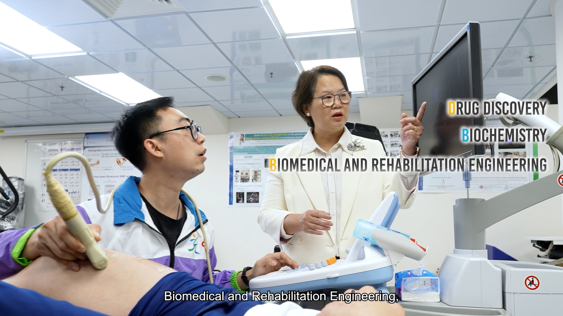 A doctor explains a medical scan on a monitor to a technician performing an ultrasound on a patient. Three text labels read Drug Discovery, Biochemistry, and Biomedical and Rehabilitation Engineering.