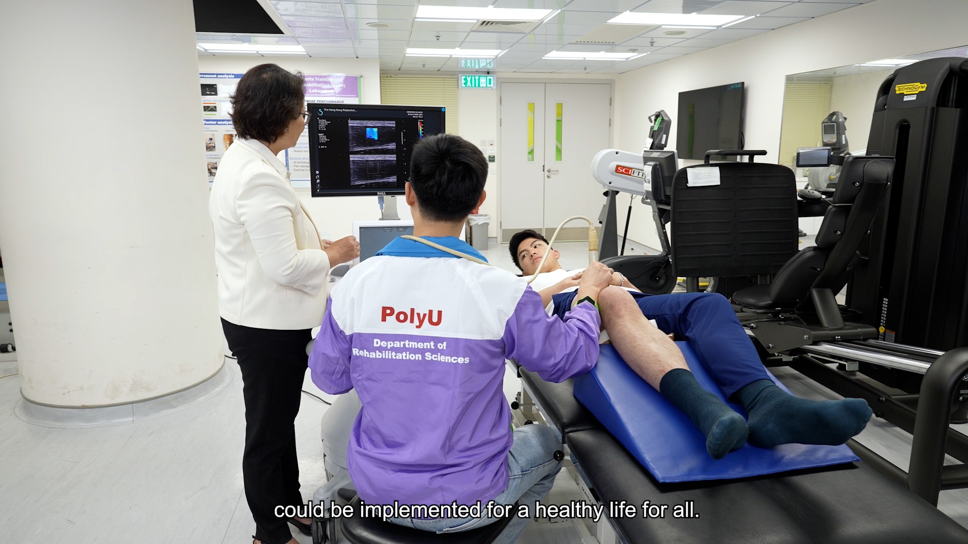 A person lies on an examination table with sensors on their leg while two people, one in a "PolyU Department of Rehabilitation Sciences" jacket, monitor data on a screen in a clinical setting. Subtitles read: "could be implemented for a healthy life for all.