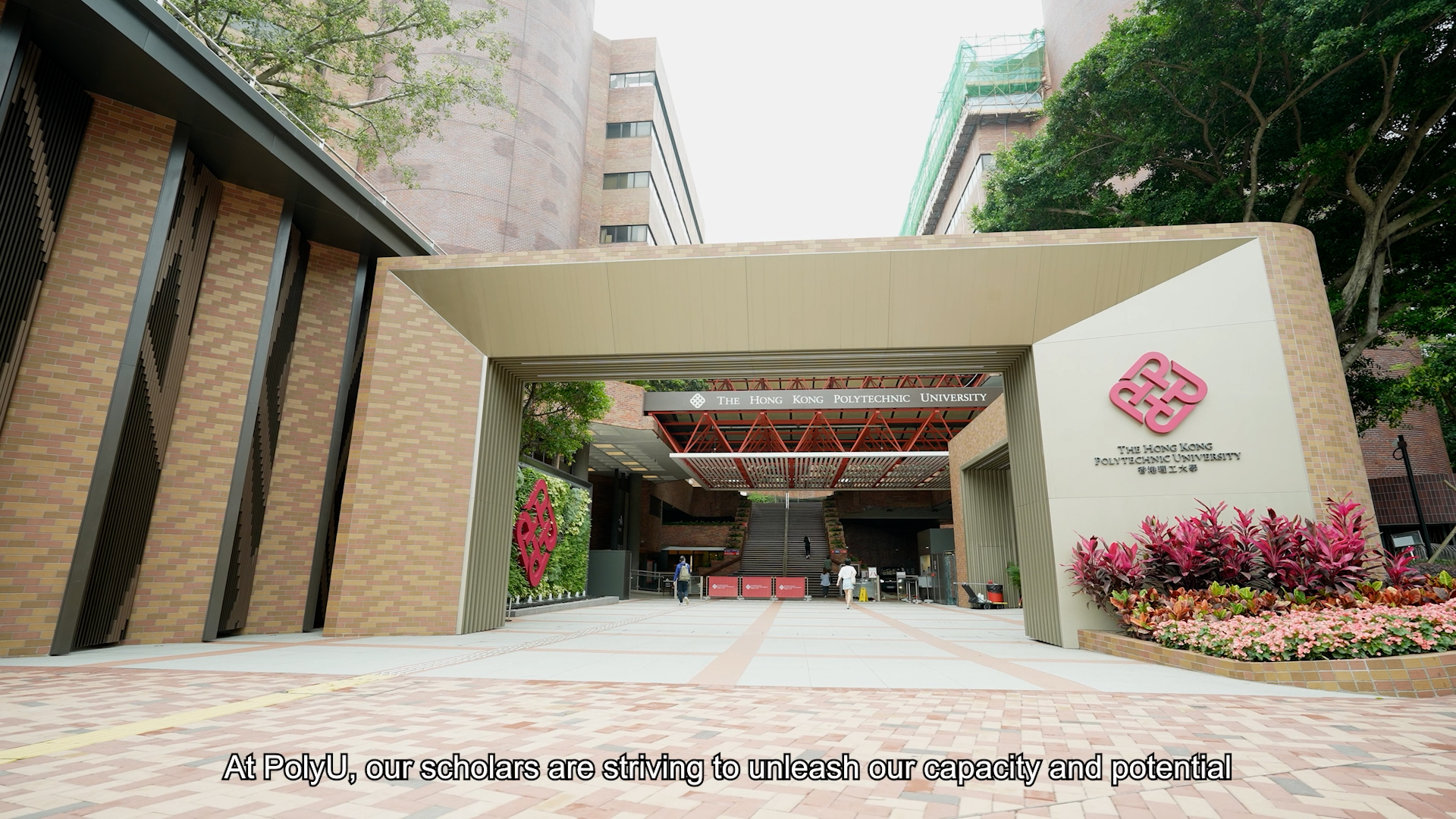 Entrance of The Hong Kong Polytechnic University with a modern gate, university logo, greenery, and text on the image that reads: "At PolyU, our scholars are striving to unleash our capacity and potential.