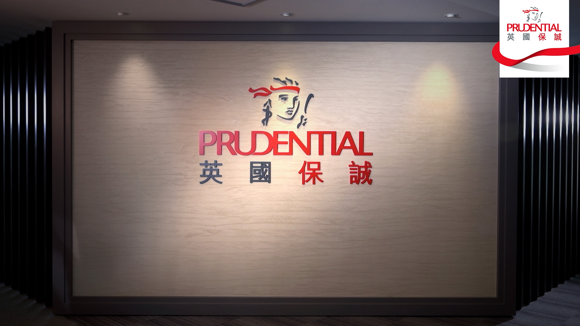 A wall sign with the Prudential logo, including a stylized woman's face, the word "PRUDENTIAL" in red, and Chinese characters below, set against a beige textured background with black panel sides.