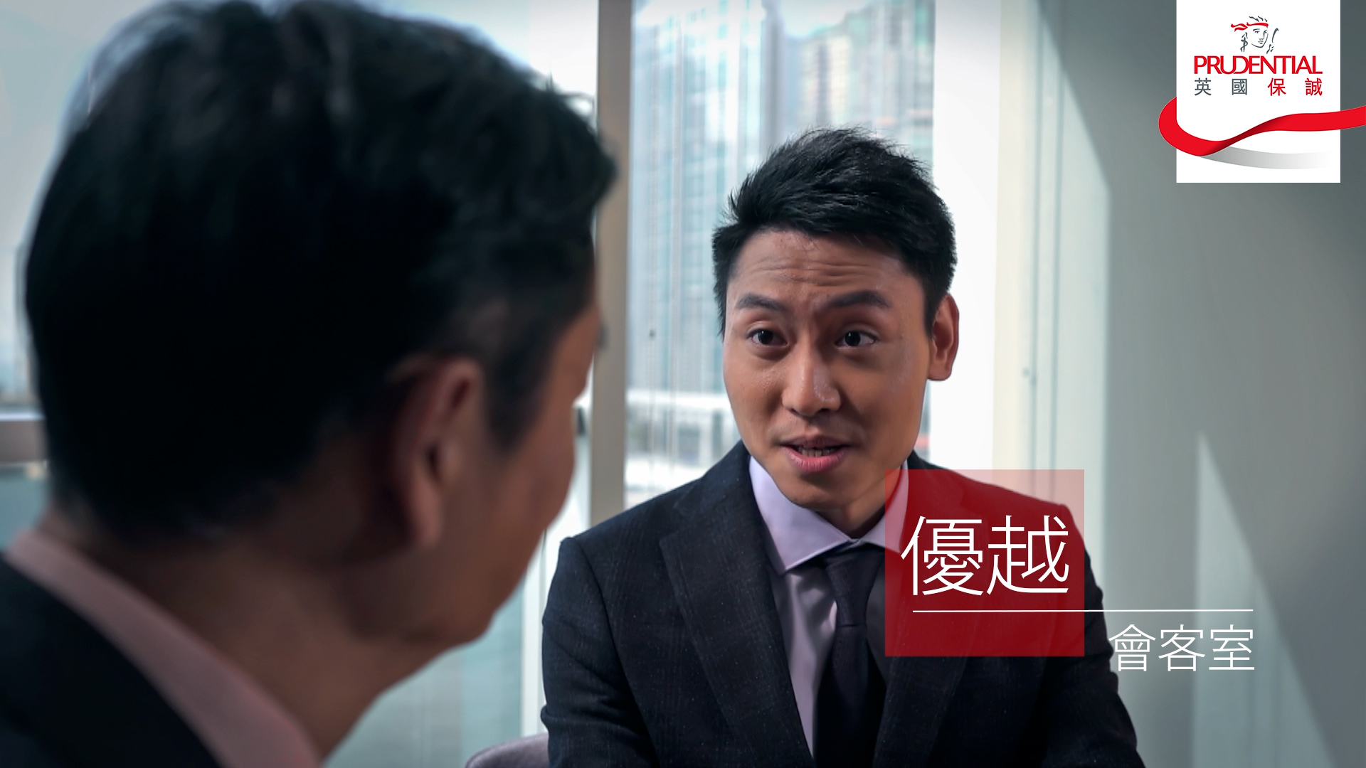 Two men in business suits are having a conversation in an office with large windows. The Prudential logo is in the top right corner. Chinese text is displayed on the right side of the image.