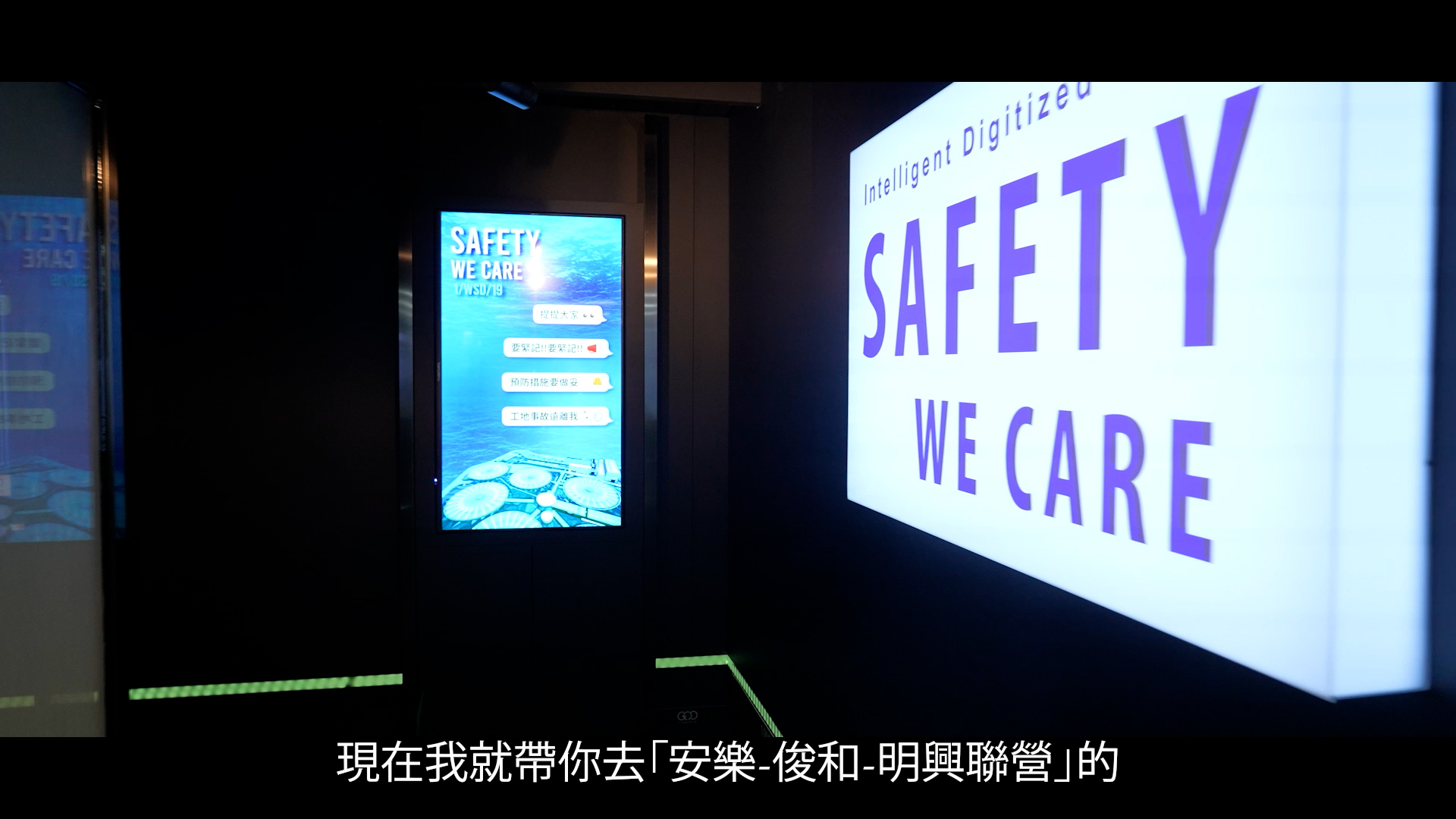 A digital sign and a wall projection both display the words "Safety We Care" in English. Chinese subtitles appear at the bottom of the image. The scene is indoors with a modern, high-tech design.