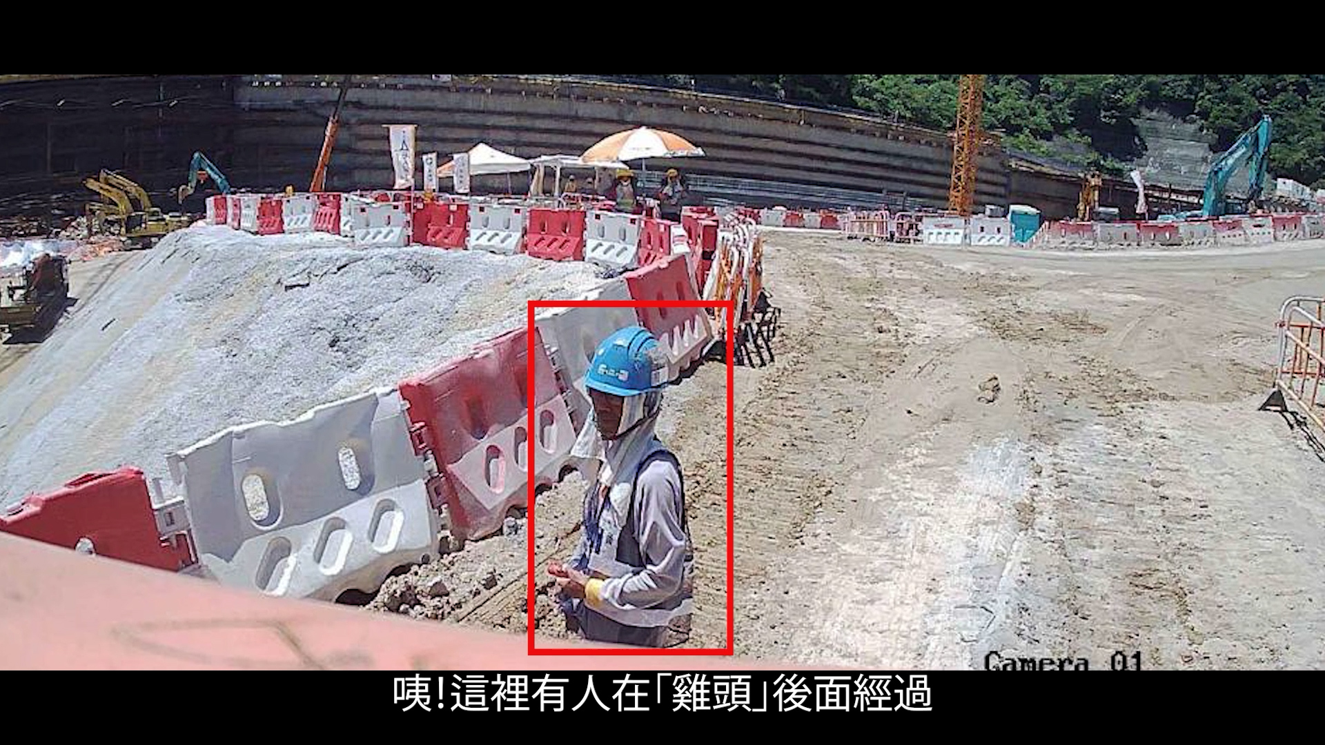 A construction worker in a helmet and mask stands near a concrete barrier at a construction site, holding equipment. The worker is highlighted by a red box, with buildings, barriers, and machinery in the background. Chinese caption at bottom.
